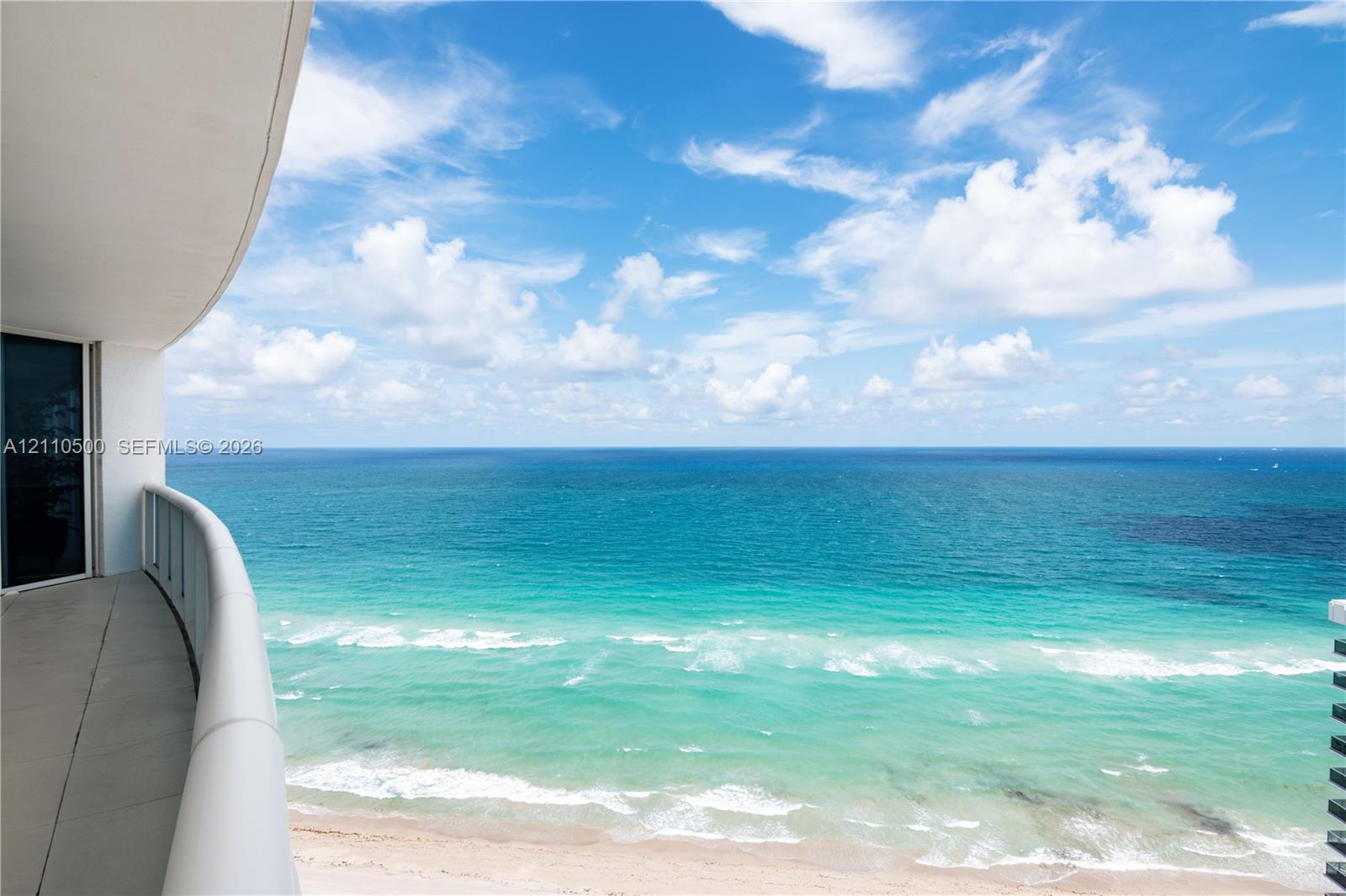 Covered balcony featuring concrete flooring and a glass-paneled railing overlooking the ocean