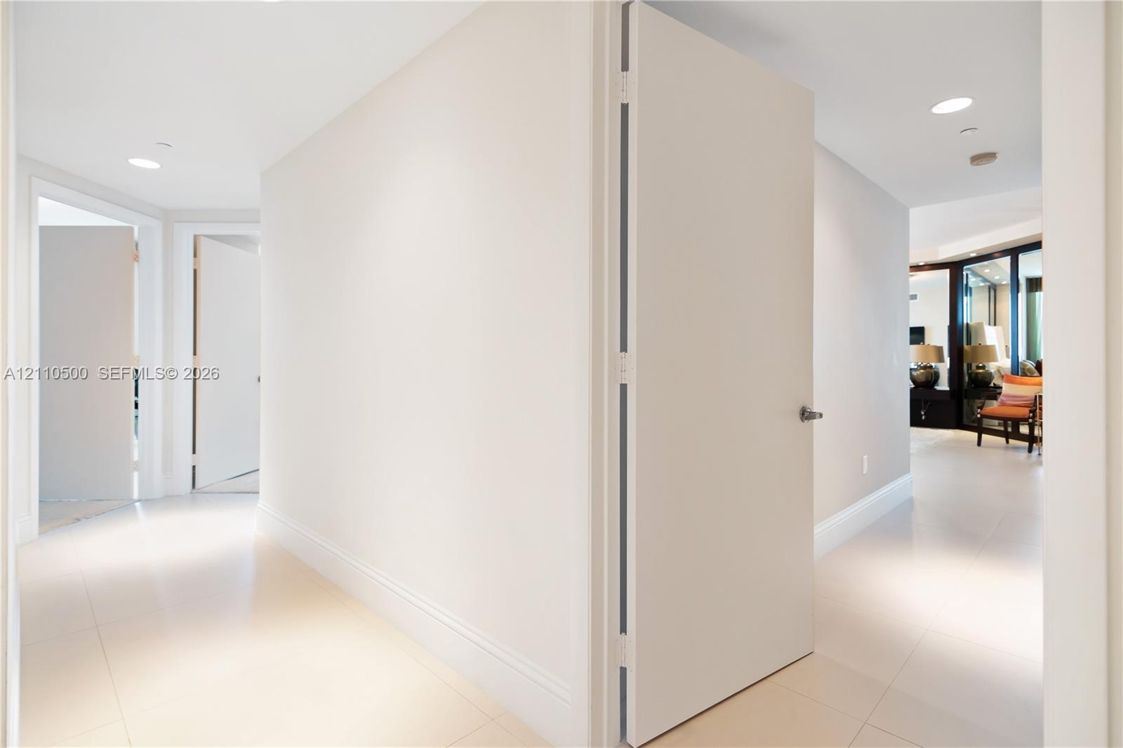 Interior hallway featuring large-format tile flooring, crisp neutral wall finishes, solid-core interior doors, and recessed ceiling lighting
