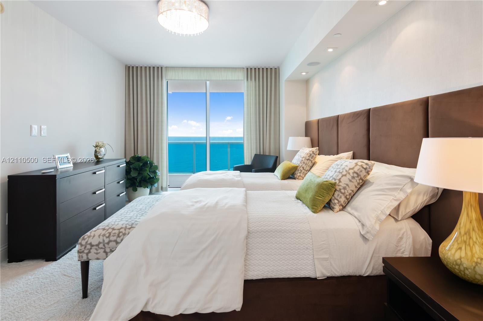 Floor-to-ceiling sliding glass doors, built-in recessed ceiling lighting, upholstered panel headboard, and neutral wall-to-wall carpeting