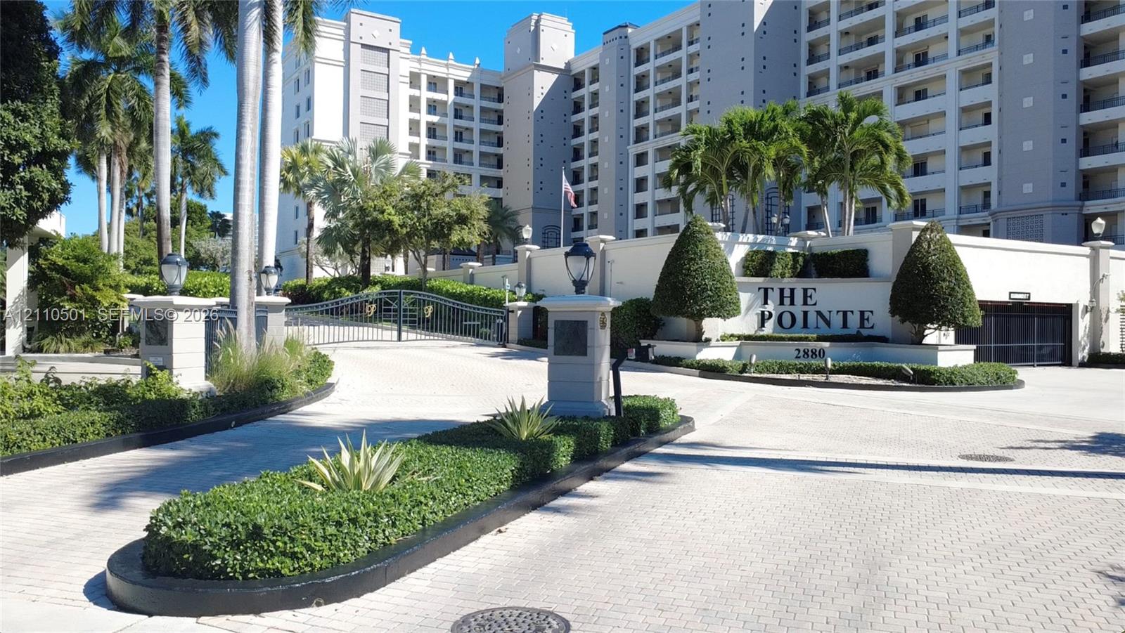 Gated entrance featuring decorative iron fencing, paved driveway, professional landscaping, and stone masonry signage
