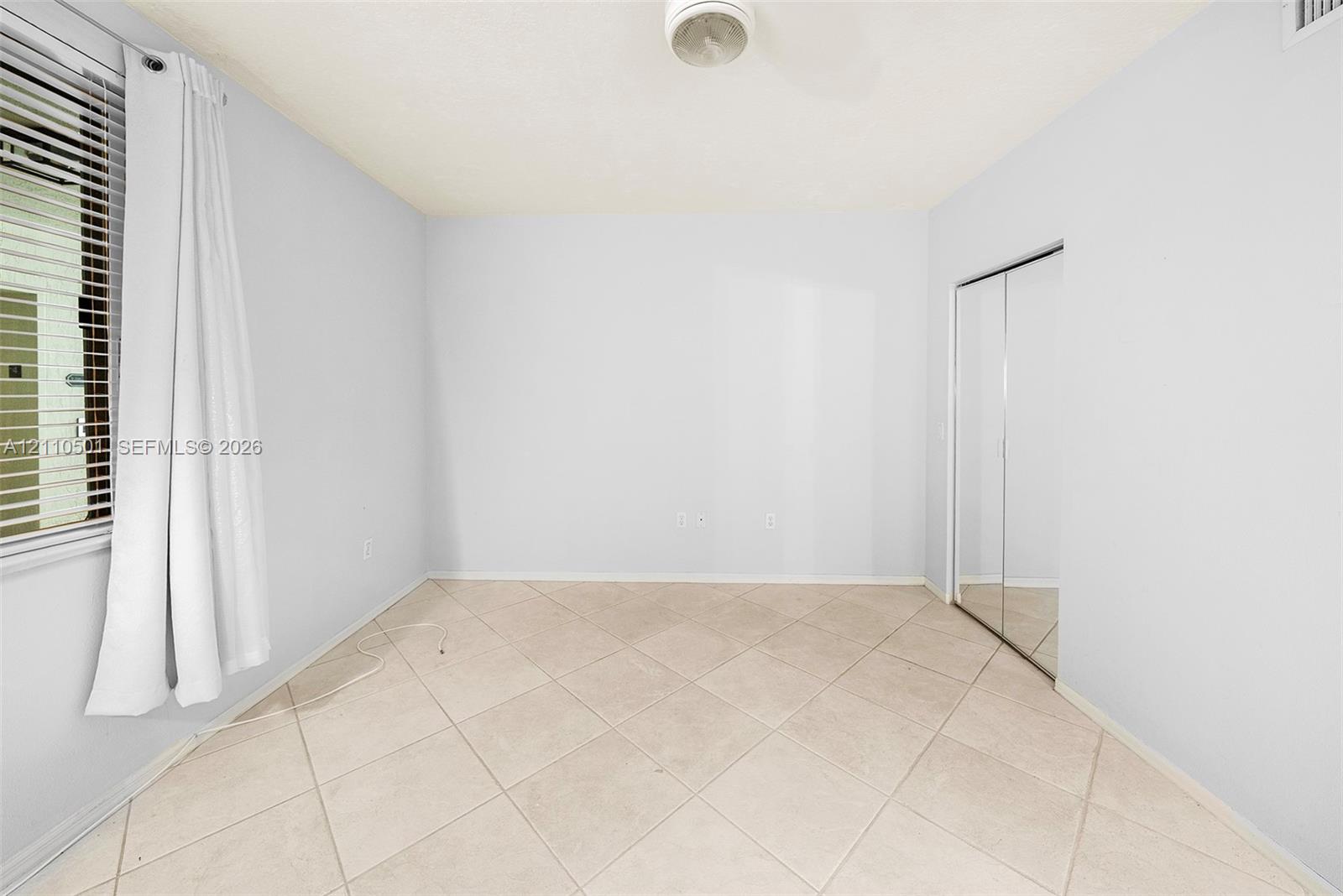 Neutral-toned room featuring ceramic tile flooring, sliding mirror-panel closet doors, and horizontal window blinds