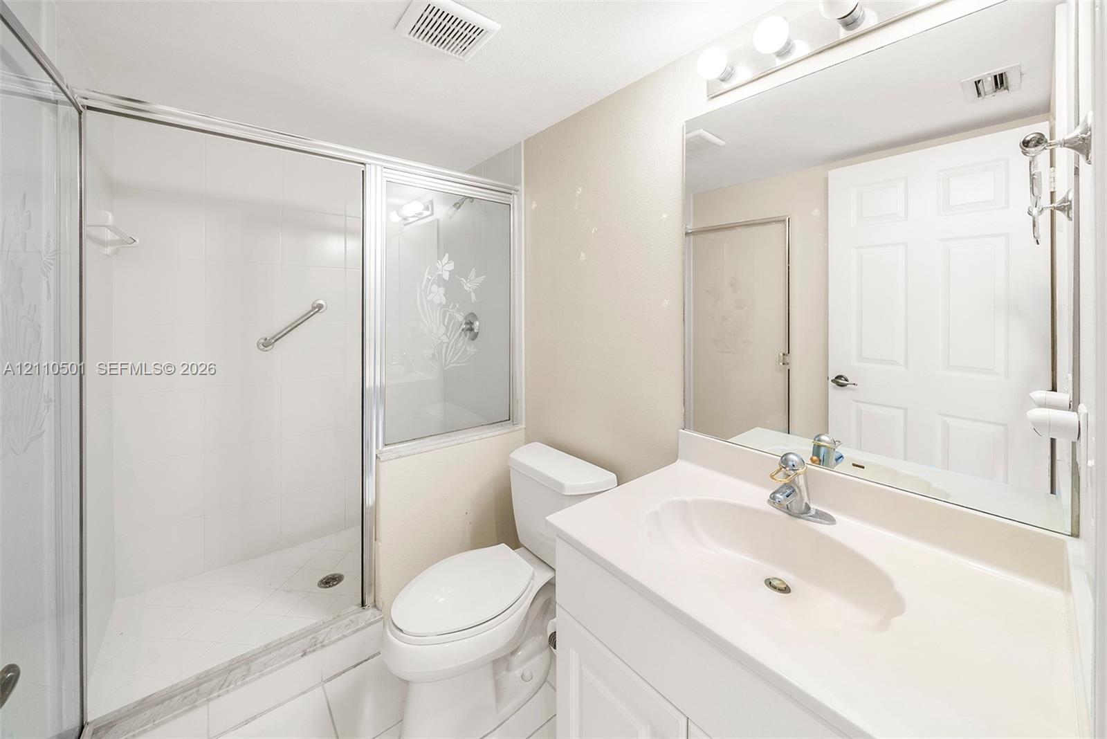 Bathroom featuring a glass-enclosed shower with etched detail, vanity with an integrated sink, polished chrome fixtures, and a large wall-mounted mirror