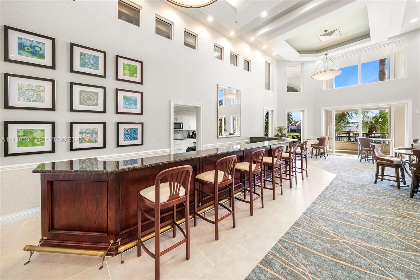 Custom wet bar featuring dark wood cabinetry, stone countertops, and a brass-tone foot rail, set within a high-ceiling space accented by coffered ceilings, multi-level windows, and recessed lighting