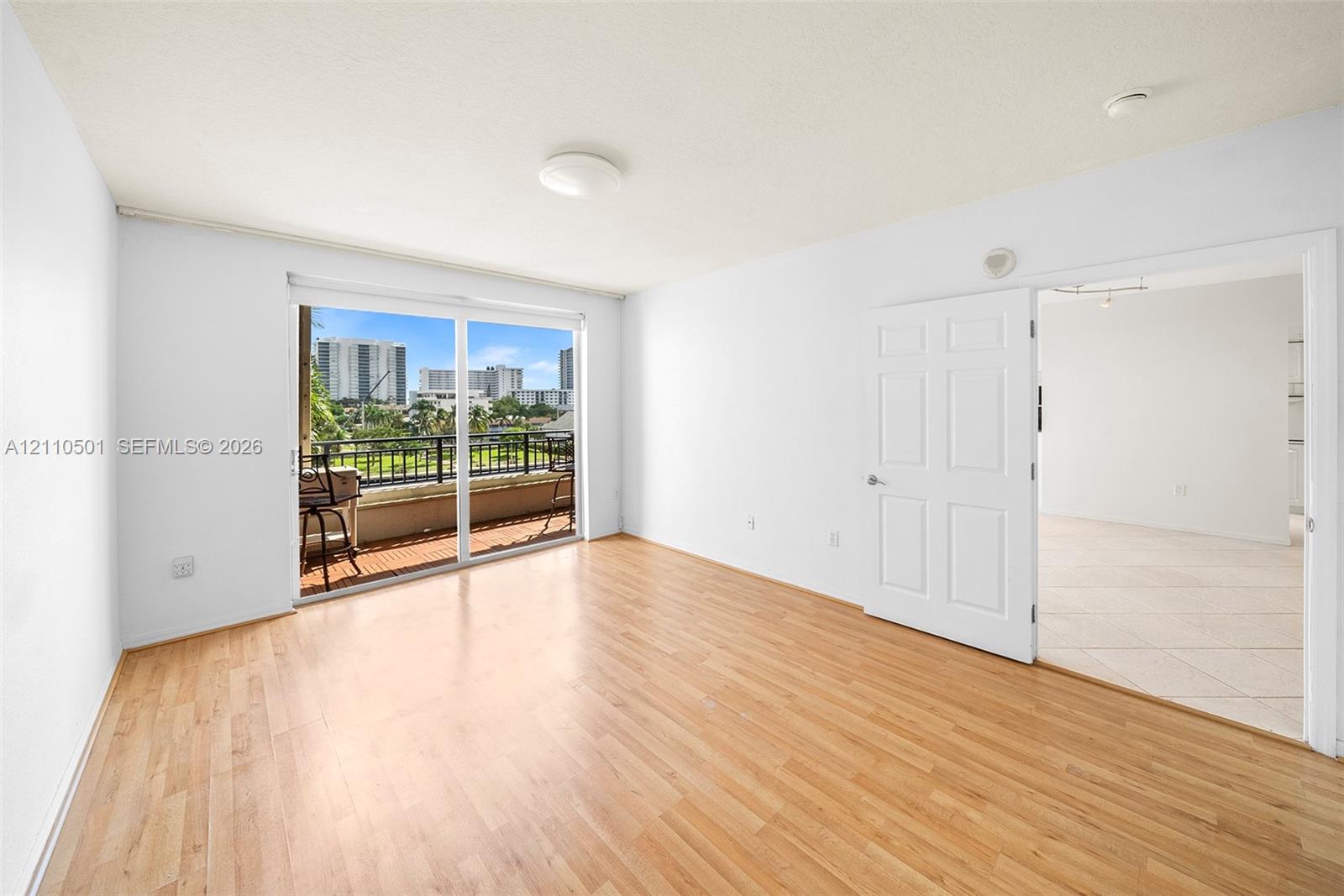 Interior space featuring light-tone wood-finish flooring, white walls, a six-panel interior door, and a sliding glass door opening to an exterior balcony