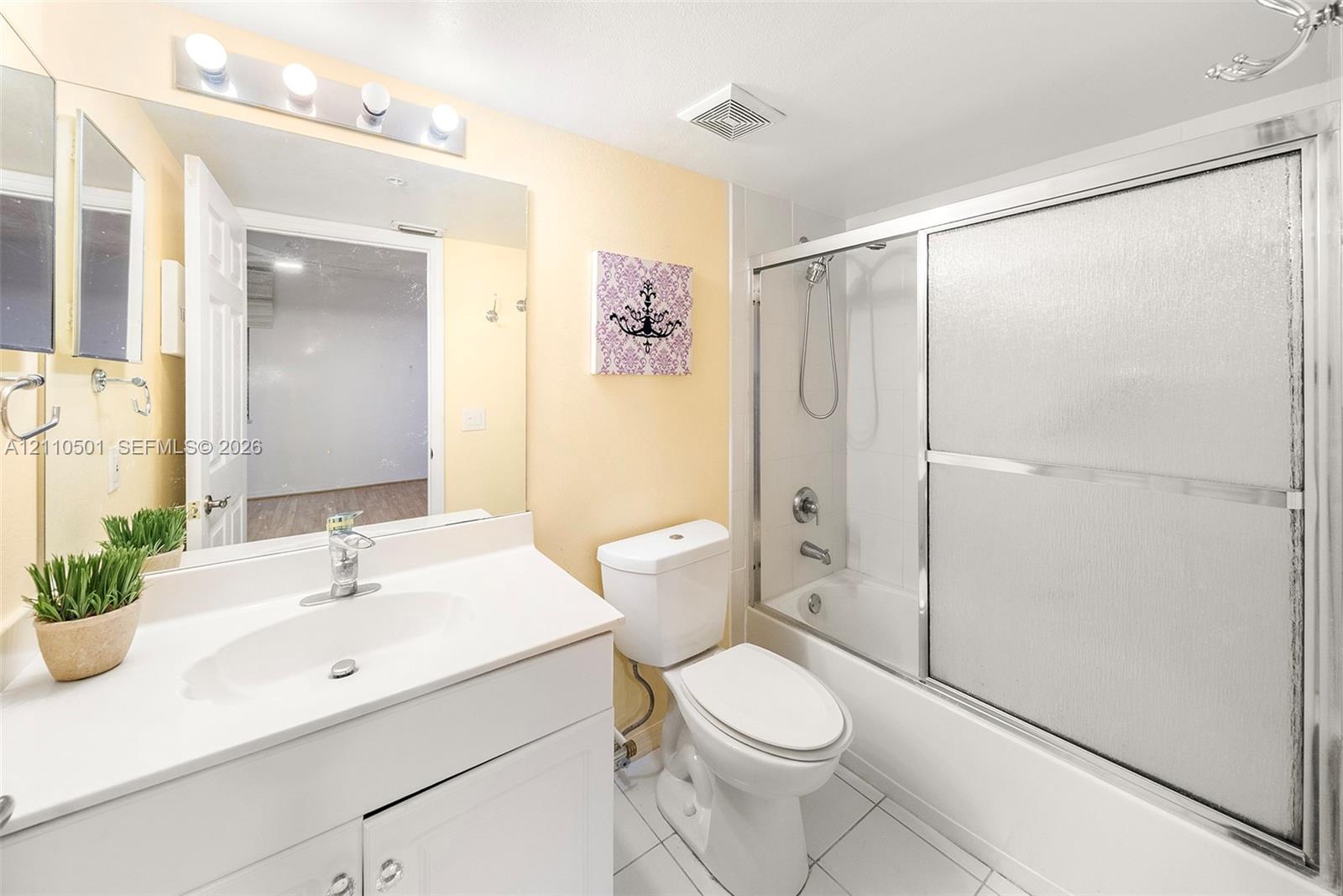 Bathroom featuring a white vanity with an integrated sink, a large wall-mounted mirror, a four-light fixture, and a tub-shower combination with sliding glass doors