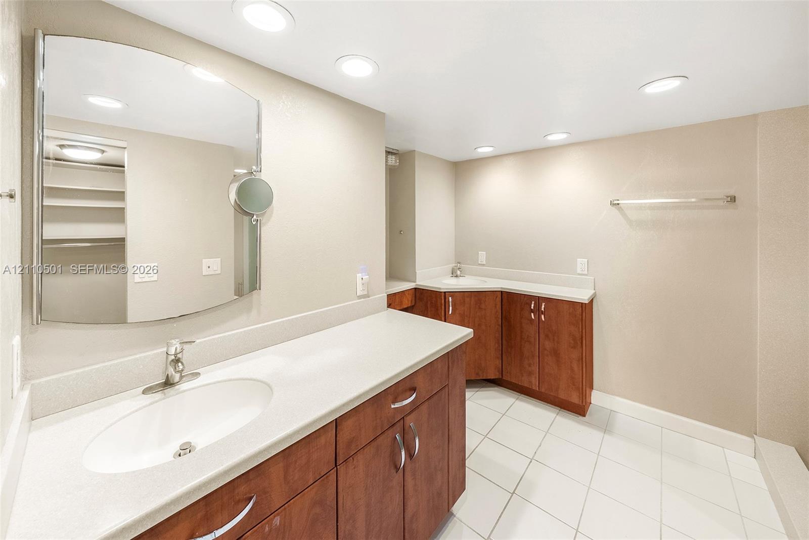Extended vanity with wood-finish cabinetry, light-toned solid surface countertops, integrated oval basins, chrome hardware, and white tile flooring