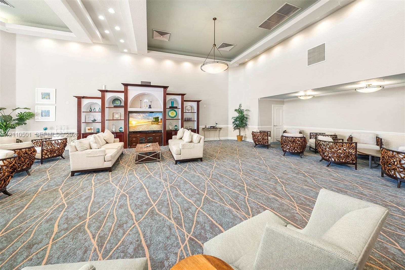 Expansive room featuring high tray ceilings, built-in recessed cabinetry with arched shelving, integrated cove lighting, and patterned carpeting