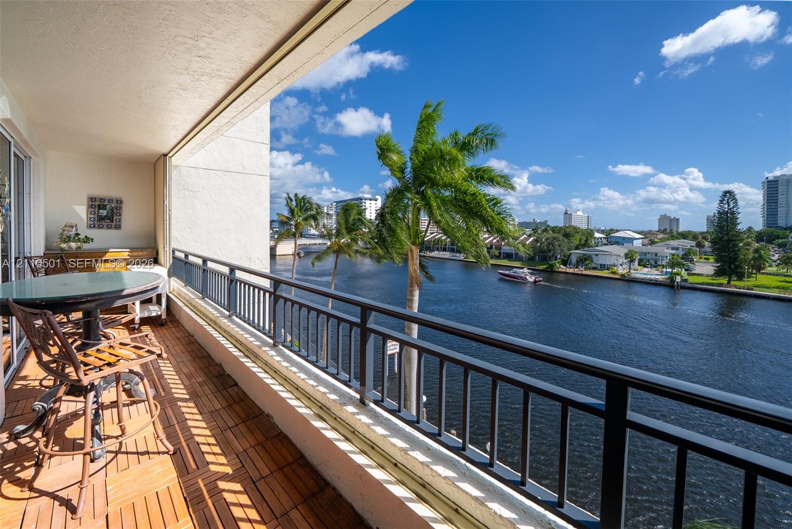 Covered balcony featuring tile flooring and metal railings, overlooking a waterway with palm trees