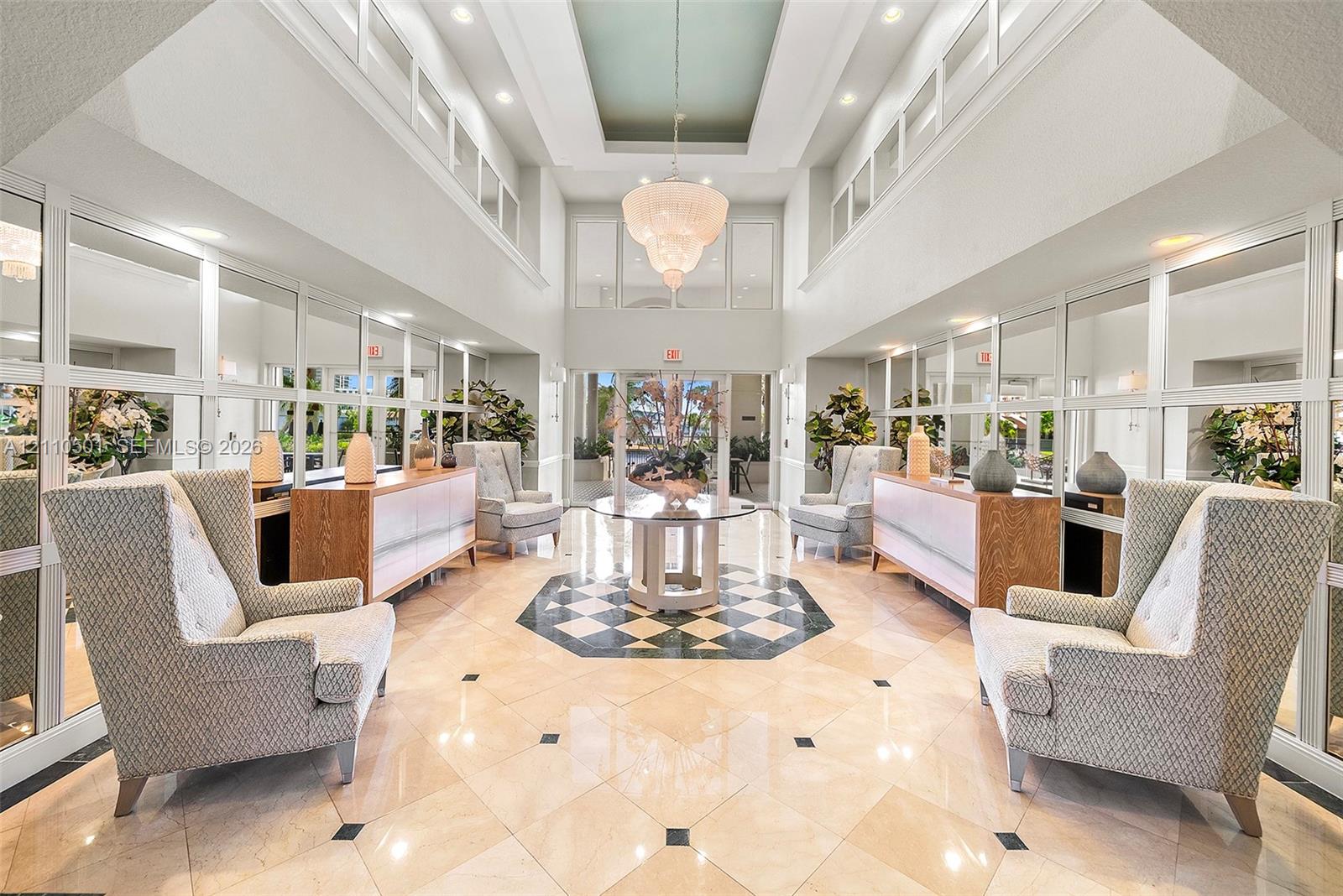 Double-height entryway featuring a tray ceiling, ornate tiered chandelier, polished stone flooring with geometric tile inlay, and floor-to-ceiling wall mirrors