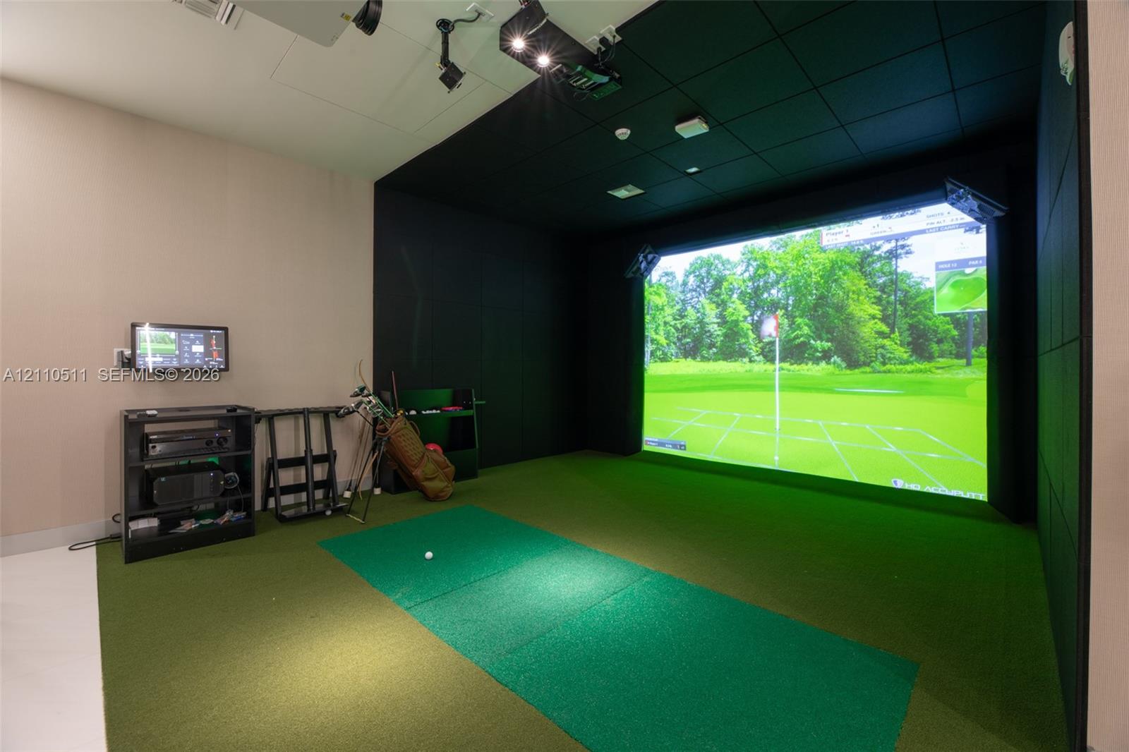 Golf simulator room featuring a large-scale projection screen, synthetic turf flooring, sound-dampening wall panels, and ceiling-mounted projection hardware
