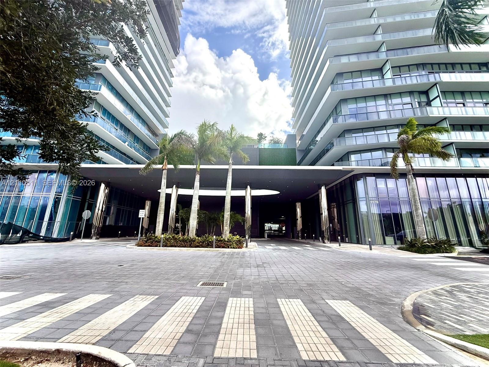 Modern high-rise exterior featuring glass-paneled balconies, floor-to-ceiling windows, a covered porte-cochre, and stone-paved motor court