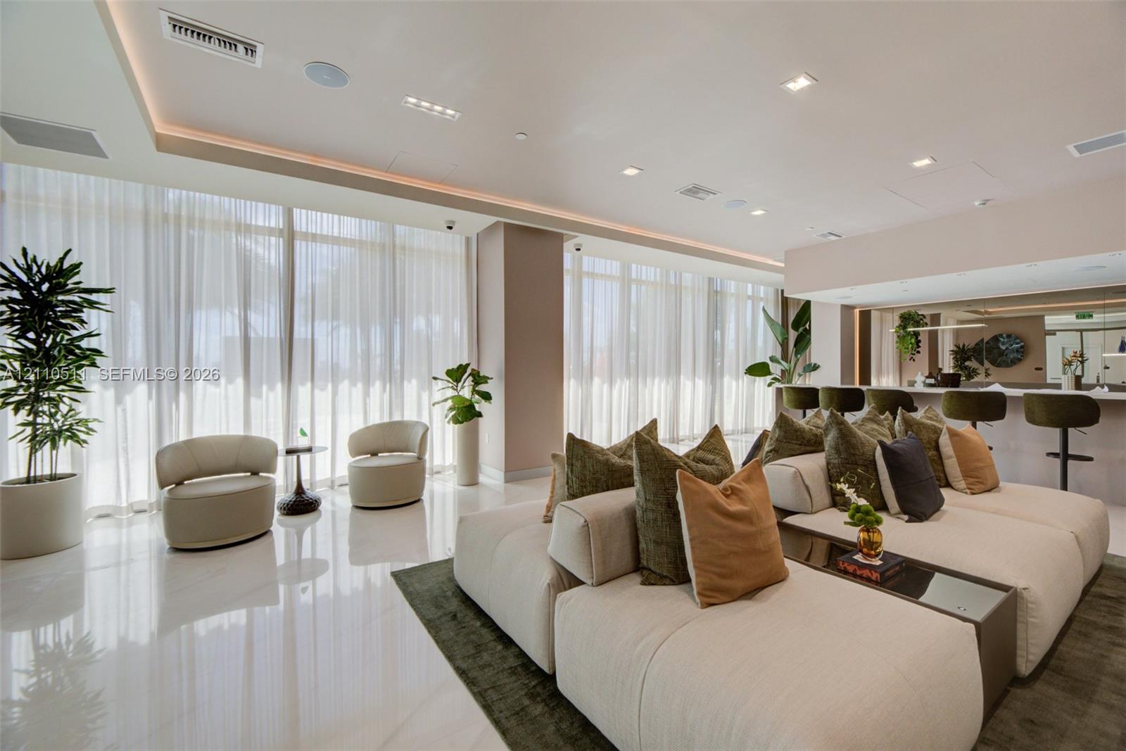 Open-concept interior featuring polished stone flooring, expansive floor-to-ceiling windows with integrated drapery tracks, recessed cove lighting, and a built-in refreshment bar