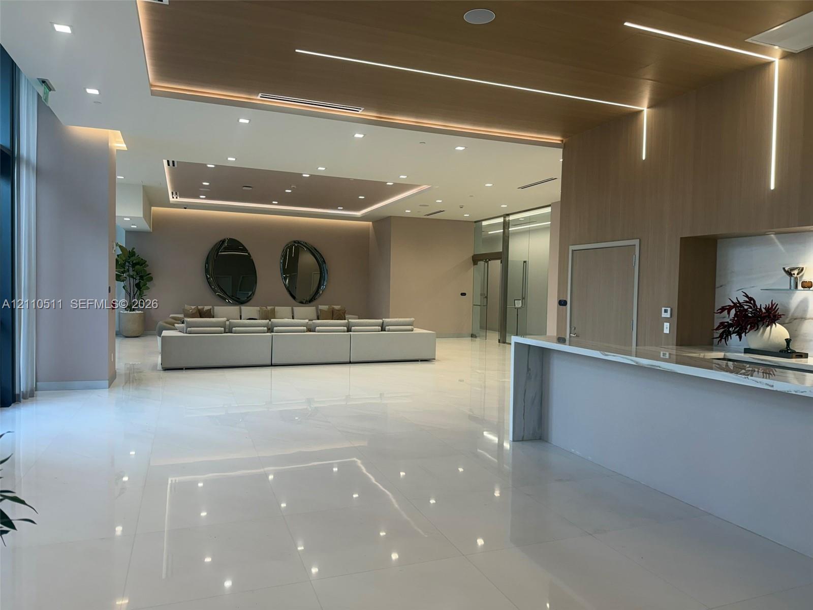 Open-concept interior featuring large-format polished tile flooring, recessed cove lighting, wood-paneled ceiling accents, and a built-in stone-top service counter