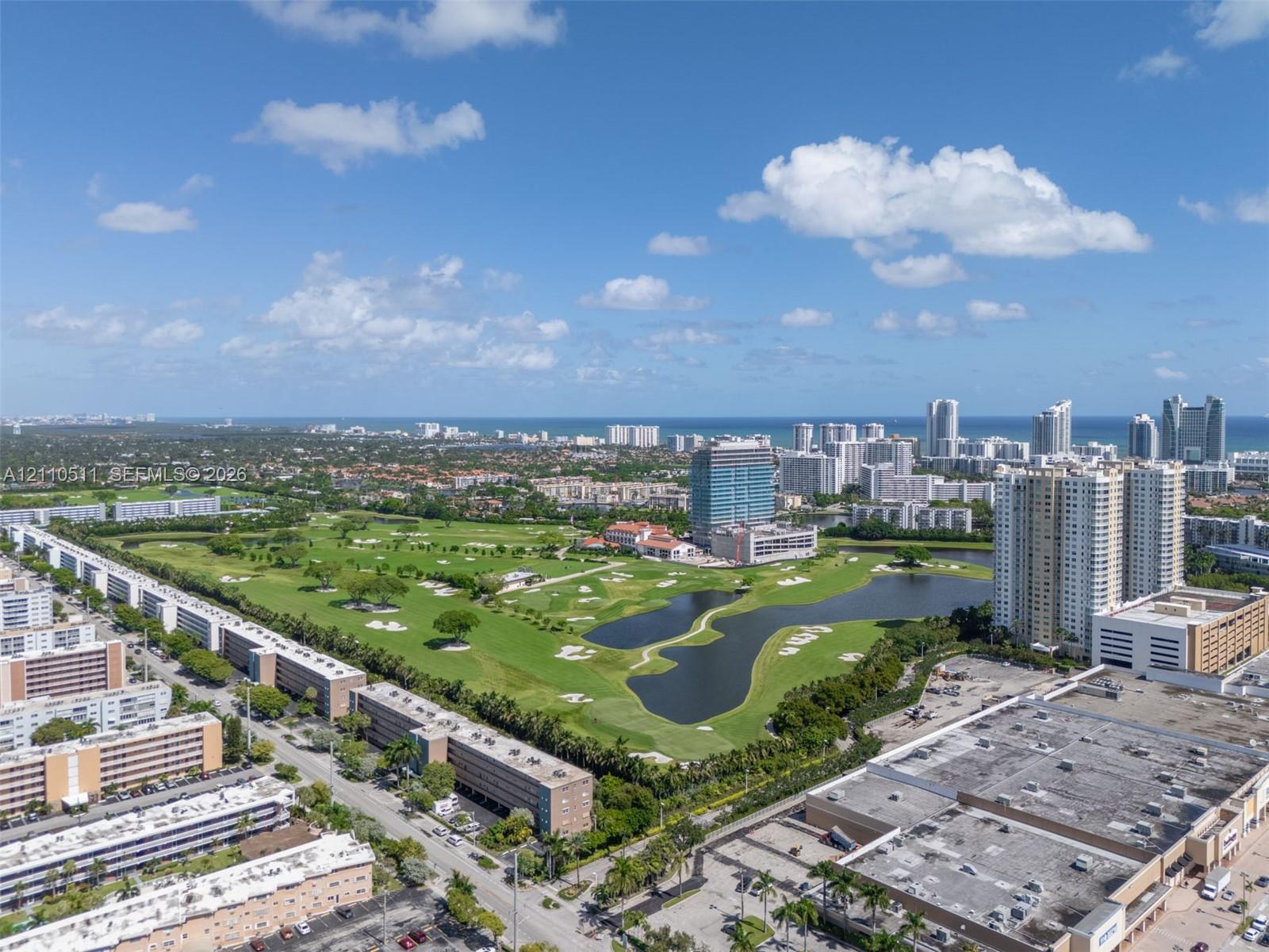Aerial perspective of a golf course featuring expansive green fairways, sand bunkers, multiple water hazards, and mature tree clusters