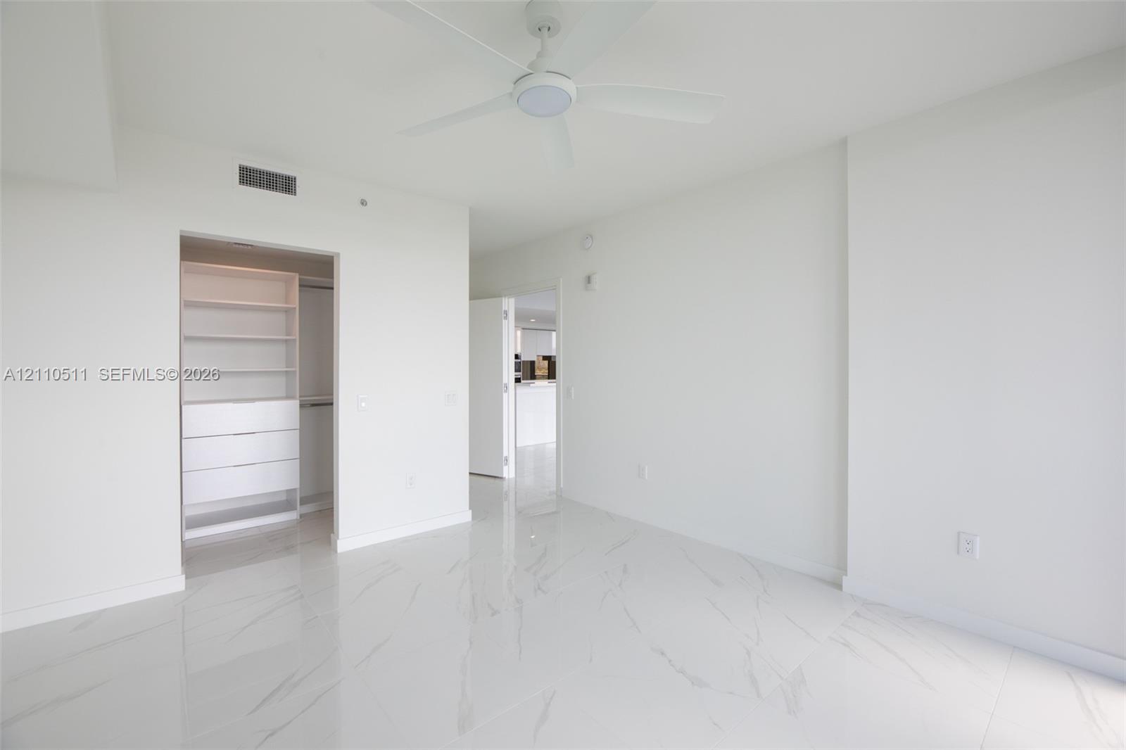 Interior space featuring white stone-finish tile flooring, ceiling fan with integrated lighting, and walk-in closet with built-in shelving and drawer units