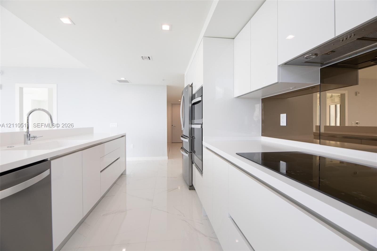 Modern kitchen featuring high-gloss white cabinetry, white stone countertops, integrated stainless steel appliances, a tinted glass backsplash, and polished tile flooring
