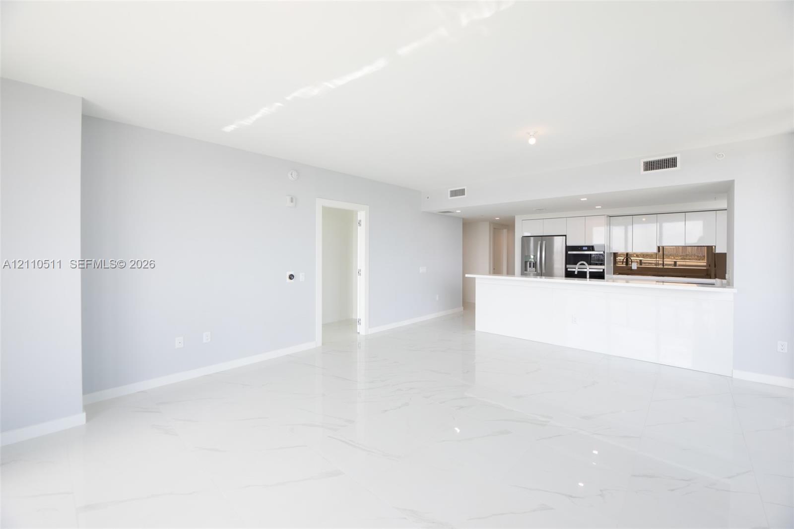 Open-concept interior featuring large-format tile flooring, white gloss cabinetry, a peninsula with a waterfall-edge countertop, and stainless steel built-in appliances