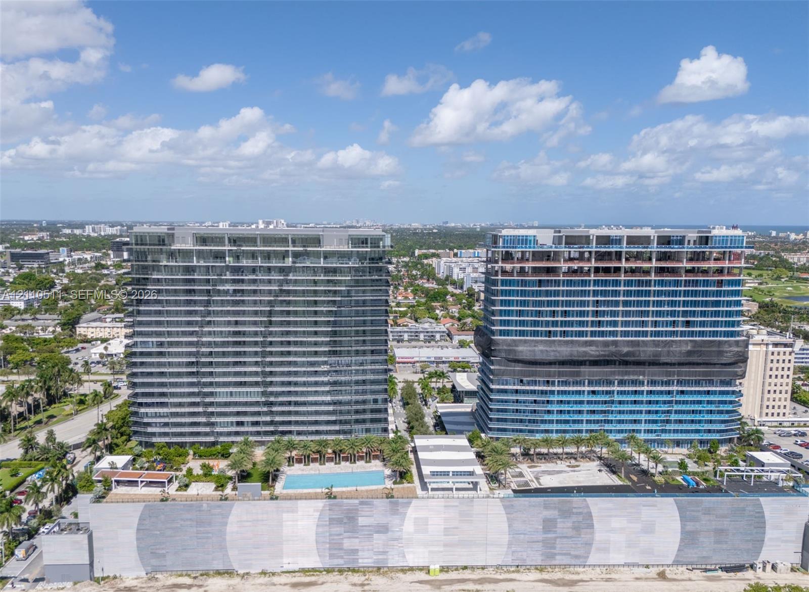 High-rise residential towers featuring expansive glass curtain wall facades, integrated swimming pool, landscaped outdoor ground-level area, and concrete perimeter retaining walls