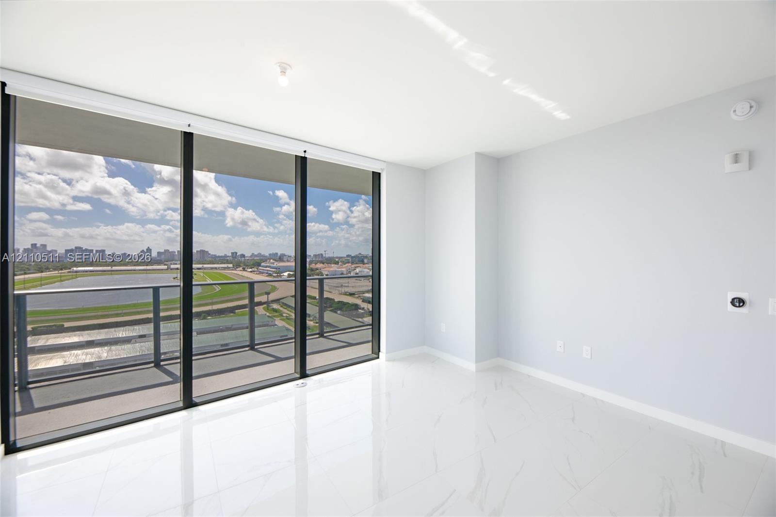 Floor-to-ceiling glass wall, private balcony with metal railing, high-gloss stone-finish flooring, and expansive urban scenery