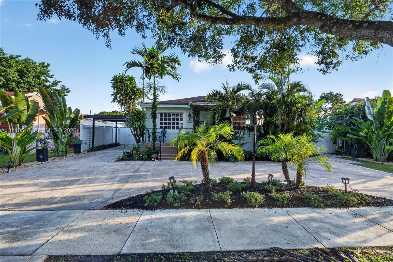 Exterior facade featuring a covered entryway, paved driveway, carport, and landscape elements including palm trees and mulched garden beds Exterior facade featuring a covered entryway, paved driveway, carport, and landscape elements including palm trees and mulched garden beds