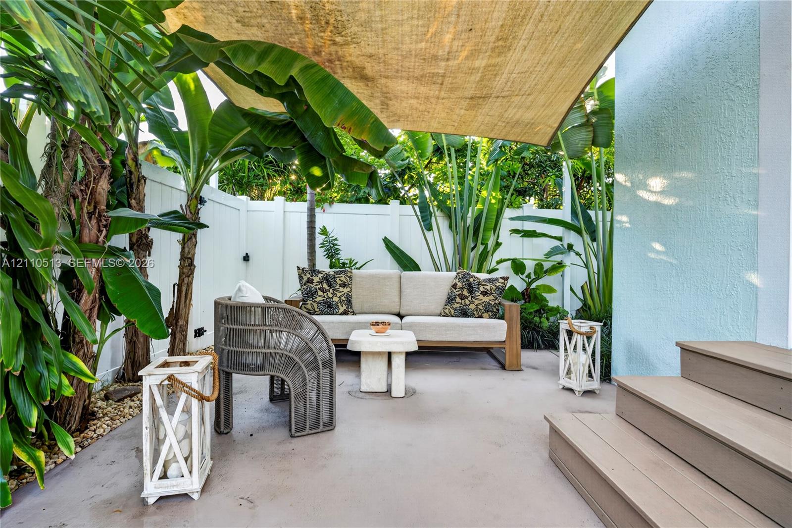 Private outdoor patio featuring a concrete surface, overhead shade sail, white vinyl privacy fencing, and exterior composite steps