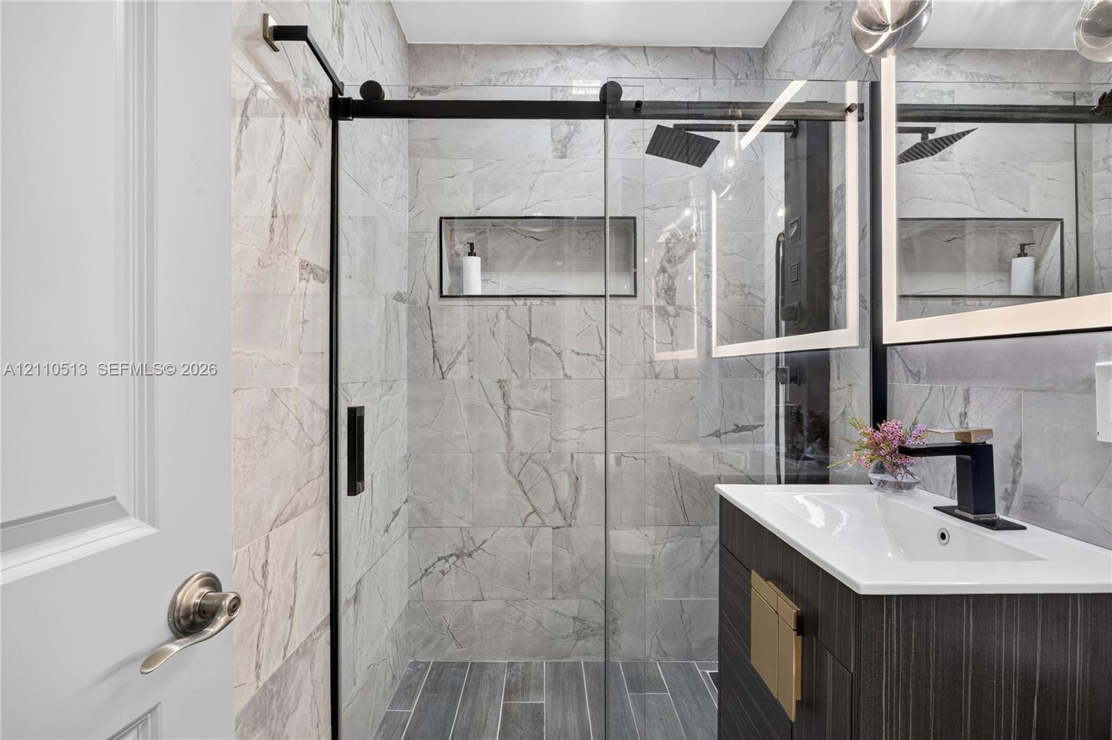 Walk-in shower with floor-to-ceiling large-format tile, glass sliding door, and recessed wall niche