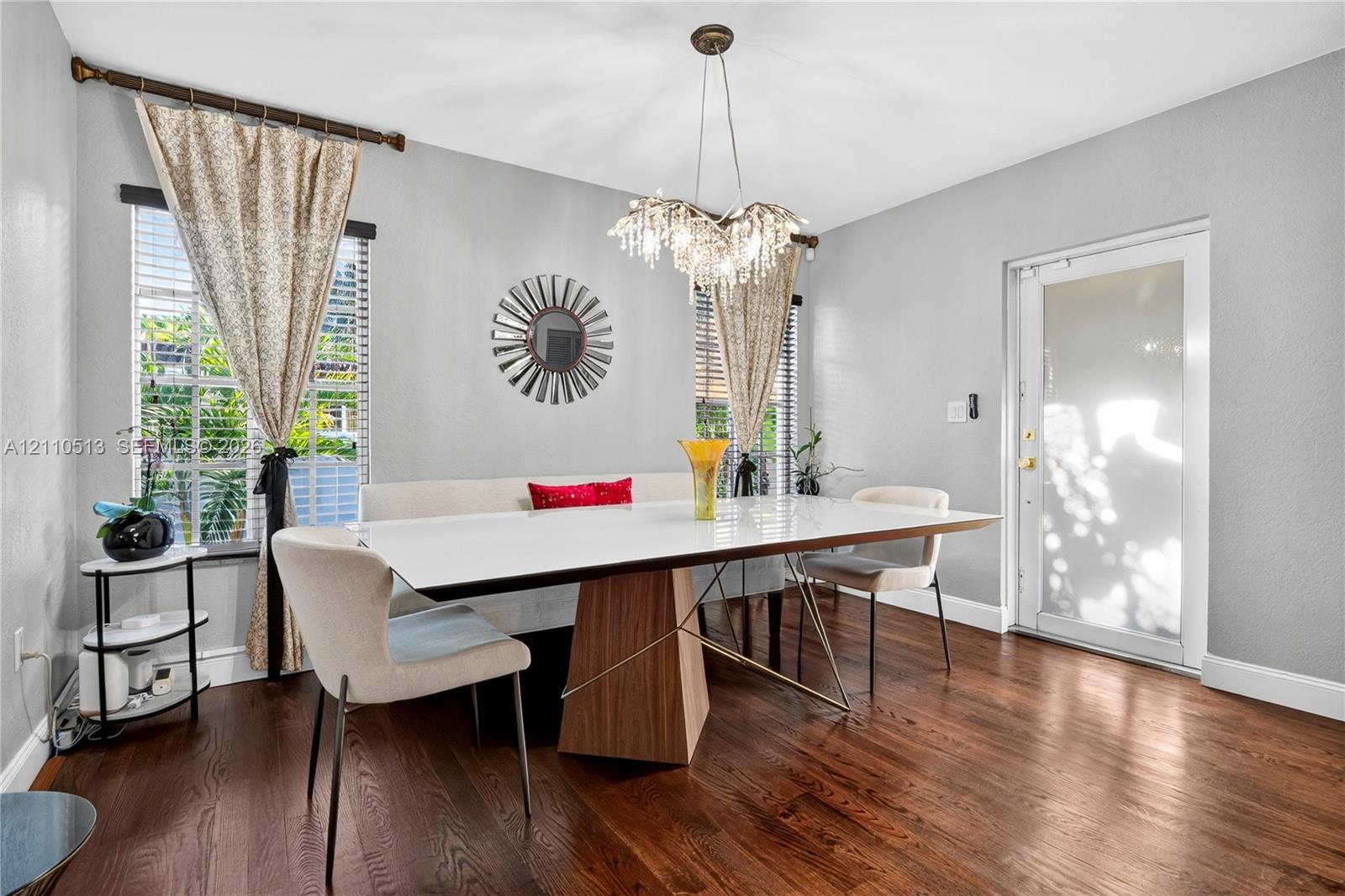 Dining area featuring wood-finish flooring, multi-pane windows with horizontal blinds, a decorative multi-light chandelier, and a glass-paneled exterior door