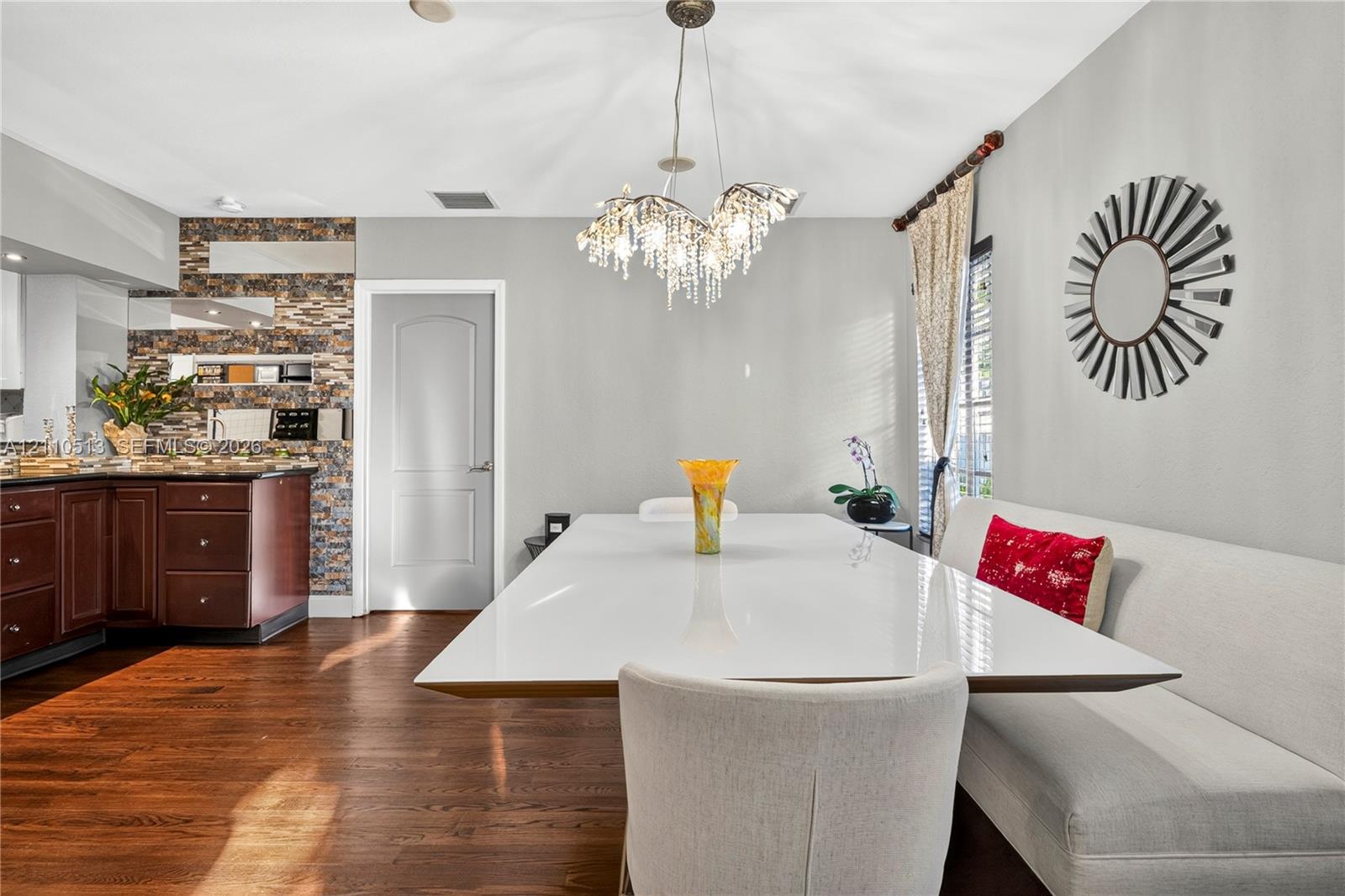 Dining area featuring wood-finish flooring, a tiered crystal chandelier, an intricate stacked-stone accent wall, and cabinetry with dark-toned finishes