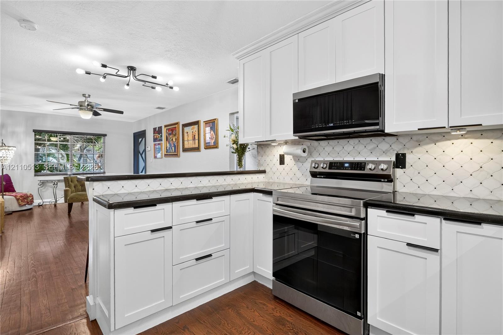 White shaker-style cabinetry, dark stone countertops, patterned tile backsplash, stainless steel appliances, and wood-finish flooring