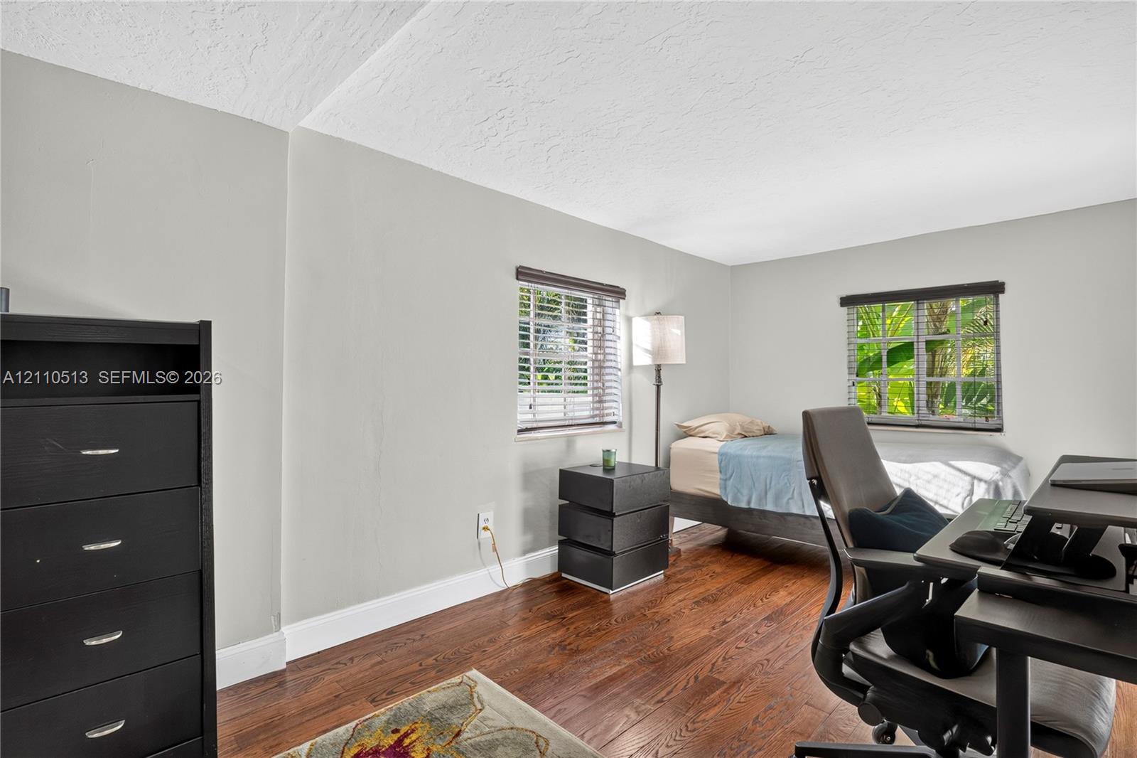 Room interior featuring wood-finish flooring, two windows with horizontal blinds, and neutral wall tones