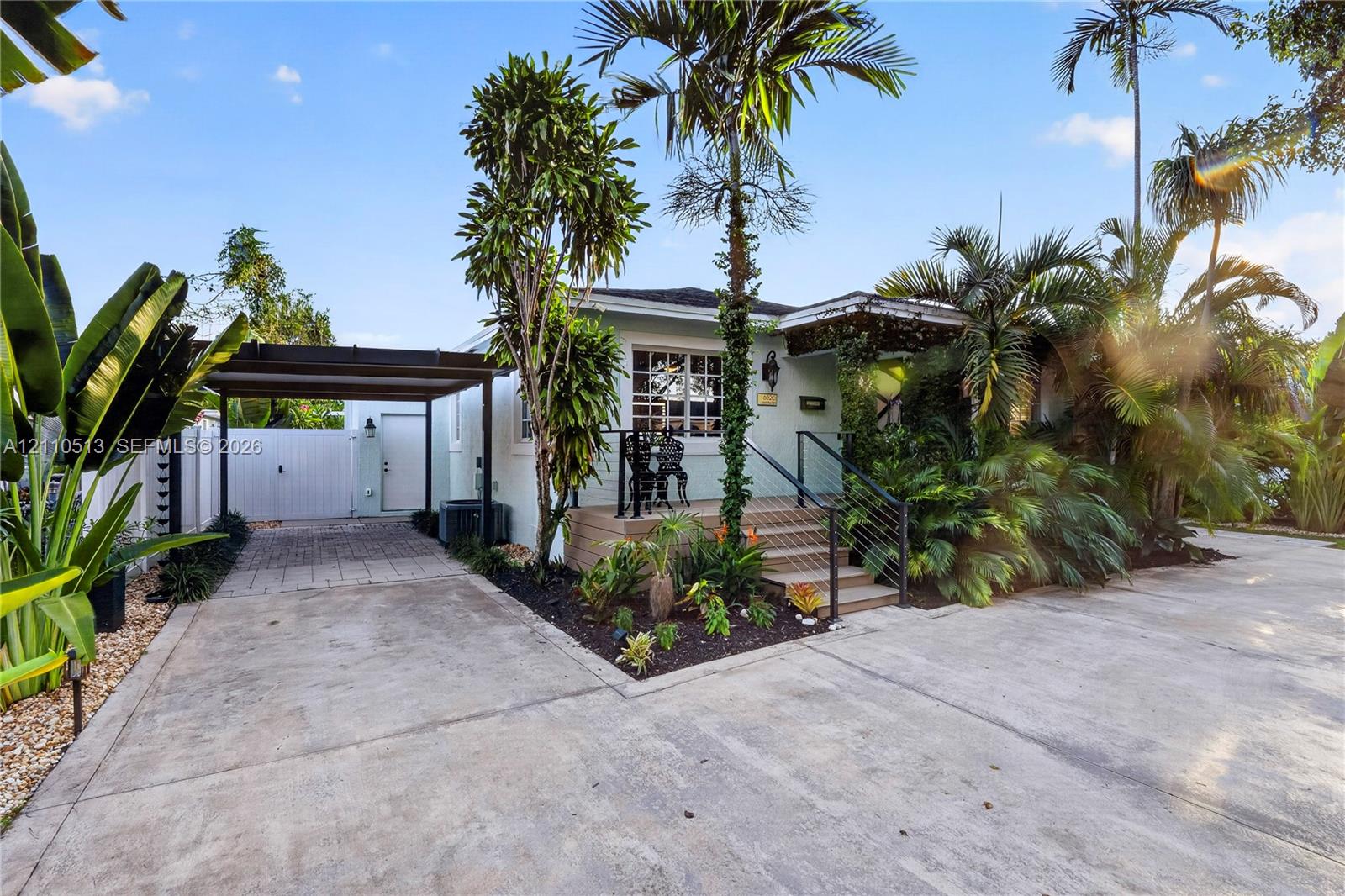 Exterior featuring a covered carport, raised wooden entryway deck, metal cable railing, and tropical landscaping