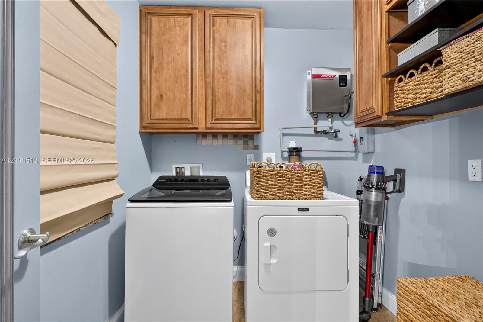 Laundry room featuring wood-finish wall-mounted cabinetry, integrated open shelving, and a tankless water heater