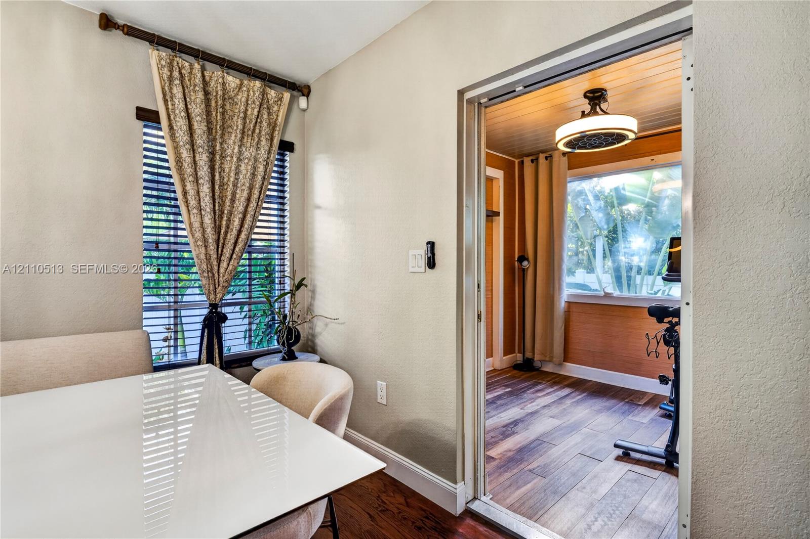 Interior space featuring wood-finish flooring, horizontal window blinds, a tiered ceiling light fixture, and wood-paneled wall accents