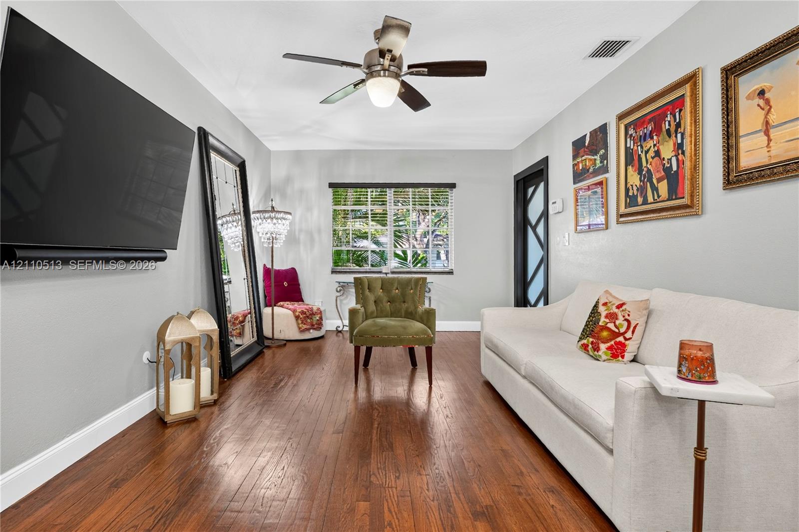 Room featuring wood-finish flooring, a multi-pane window with exterior greenery, and a ceiling-mounted light fixture with a central fan