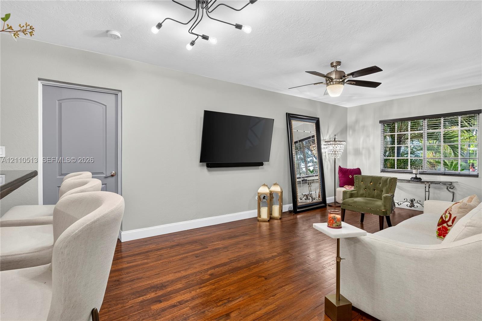 Living area featuring wood-finish flooring, a multi-arm modern light fixture, a ceiling fan, and a grid-pane window