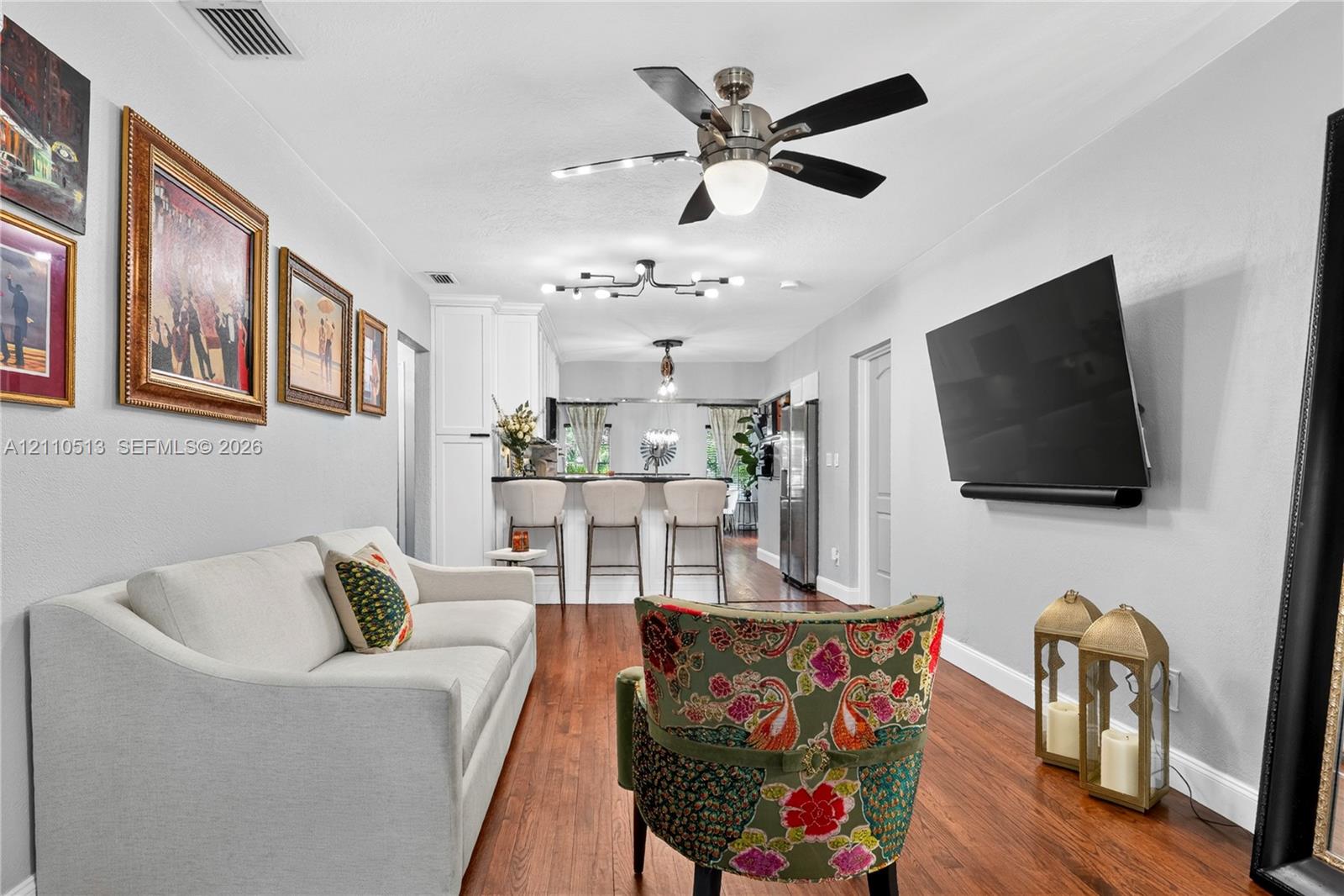 Wood-finish flooring, brushed nickel ceiling fan, multi-bulb modern chandelier, and kitchen breakfast bar with built-in cabinetry