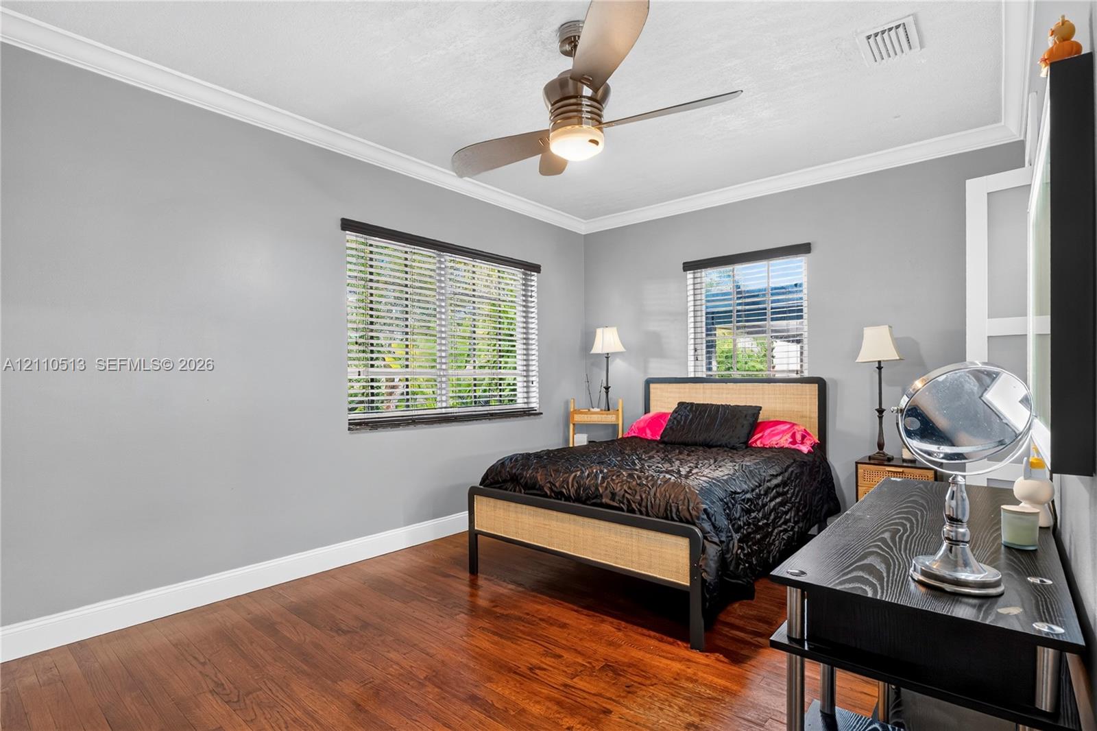 Room featuring wood-finish flooring, crown molding, dual windows with horizontal blinds, and a ceiling fan with integrated lighting