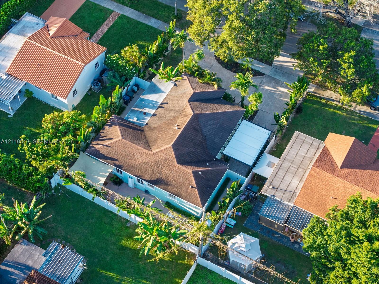 Aerial perspective of a property featuring an asphalt shingle roof, a concrete driveway, a screened-in swimming pool enclosure, and lush tropical landscaping Aerial perspective of a property featuring an asphalt shingle roof, a concrete driveway, a screened-in swimming pool enclosure, and lush tropical landscaping