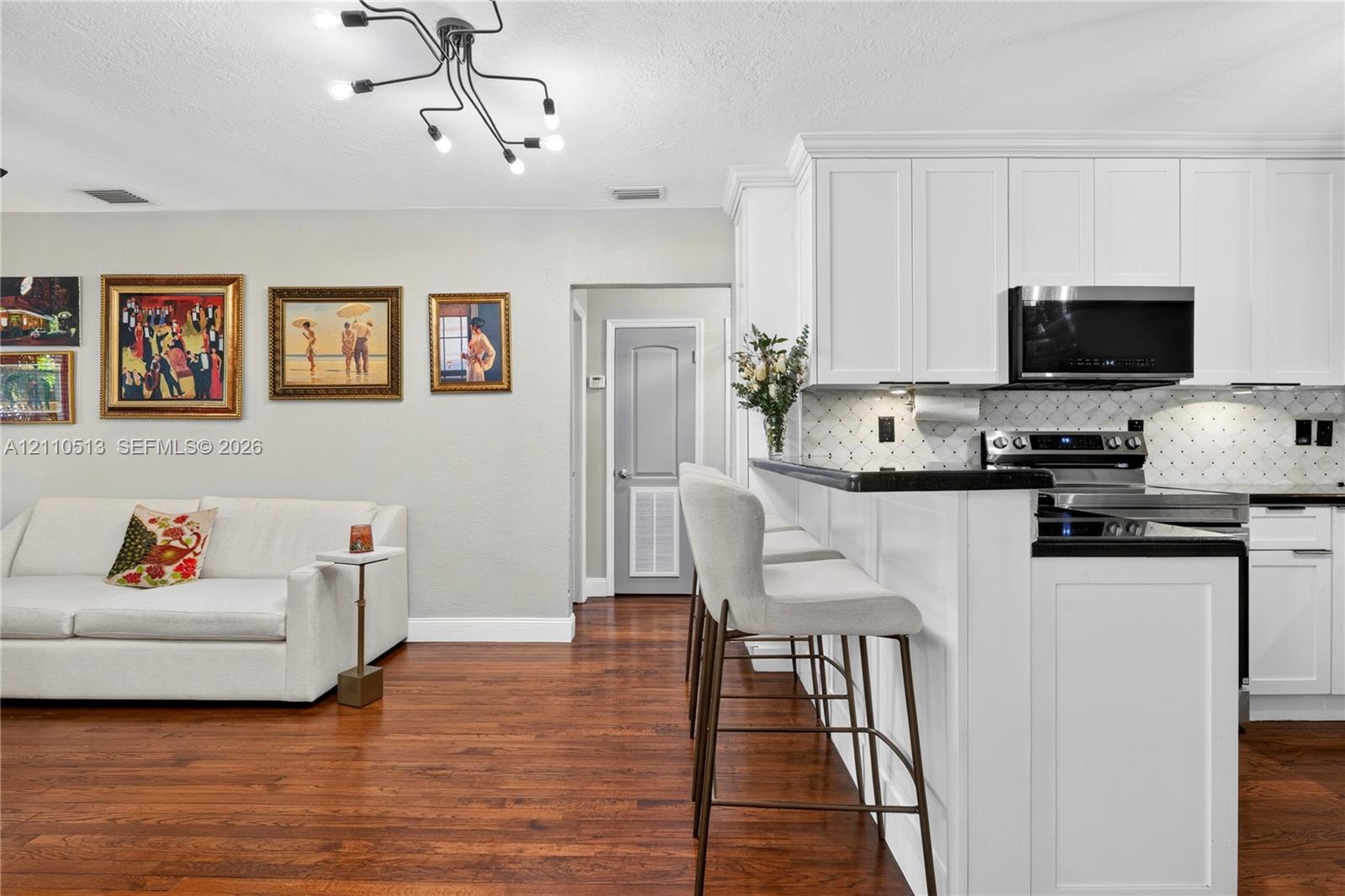Kitchen featuring white shaker-style cabinetry, dark stone countertops, a geometric-pattern tile backsplash, stainless steel appliances, and wood-finish flooring