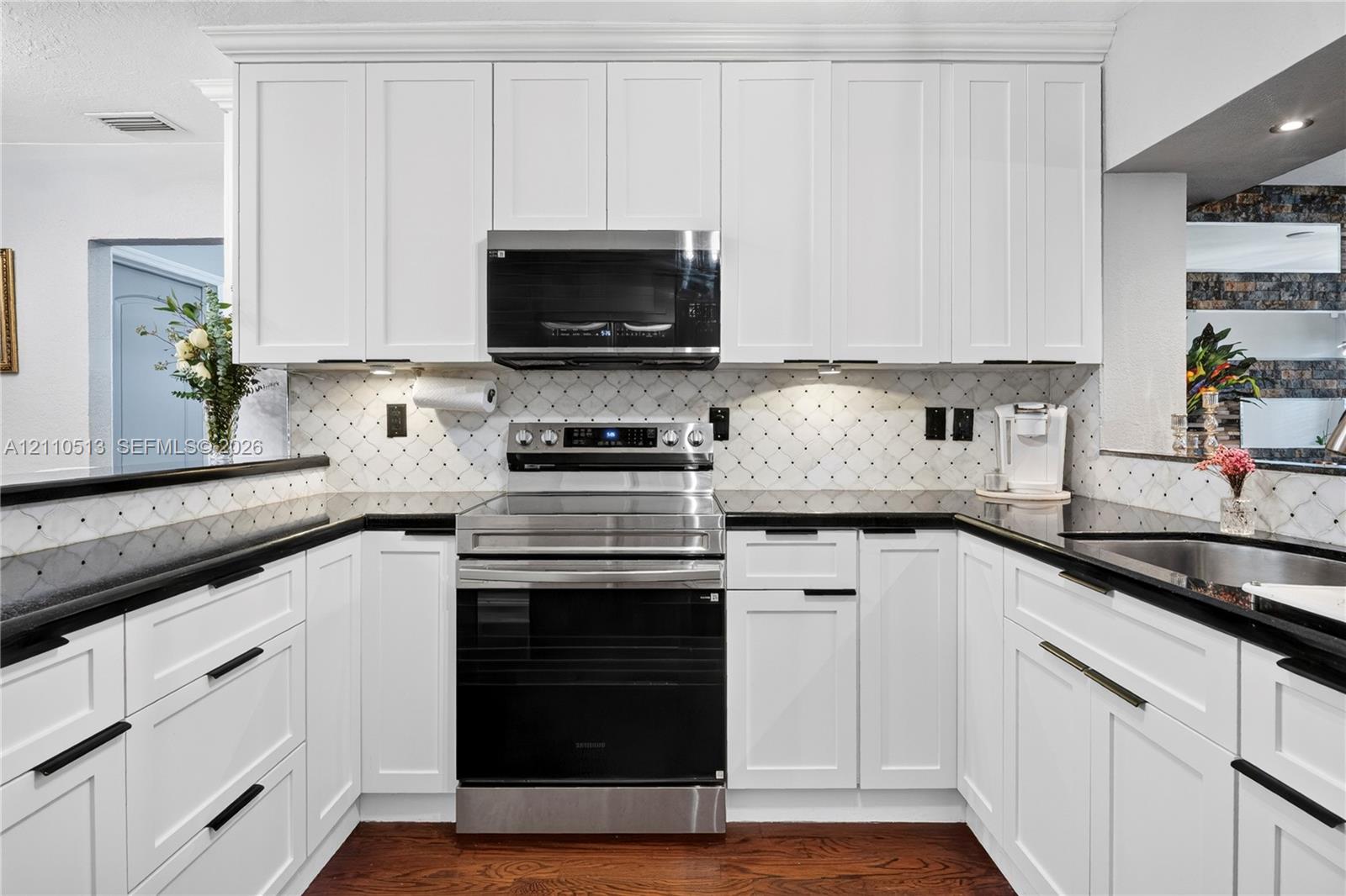 Kitchen featuring white shaker-style cabinetry, stainless steel appliances, dark stone countertops, decorative tile backsplash, and wood-finish flooring