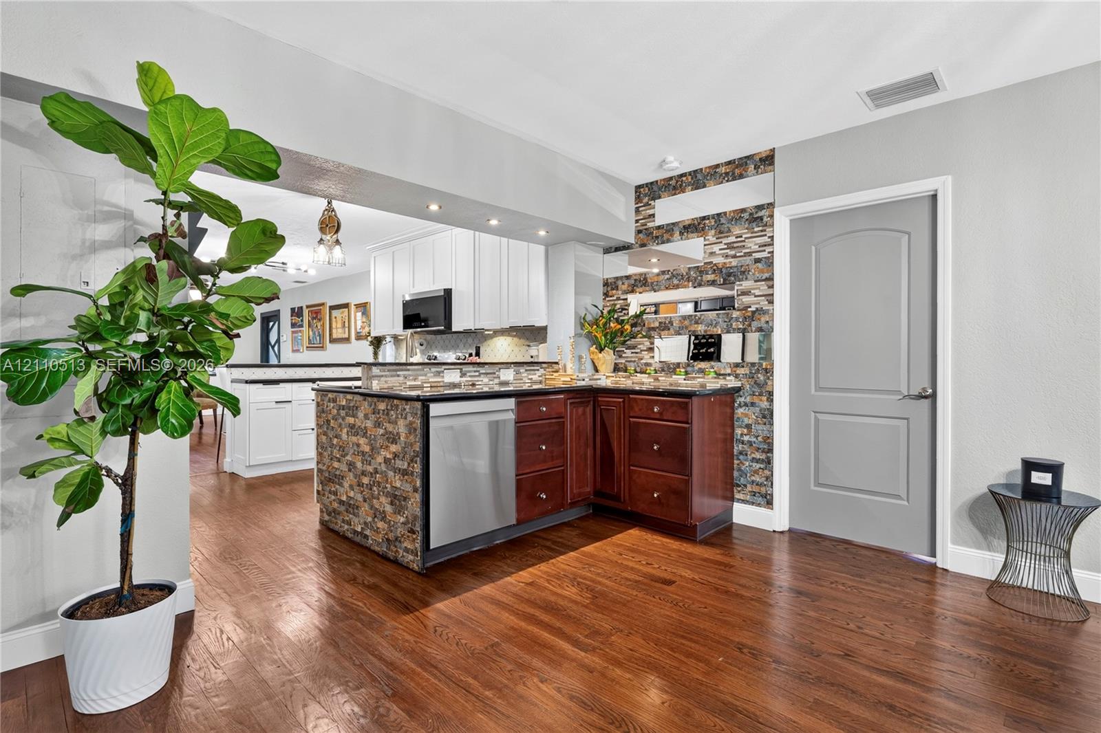 Kitchen featuring wood-finish flooring, a tiered center island with stone-veneer facing, stainless steel dishwasher, and a stone-veneer accent wall