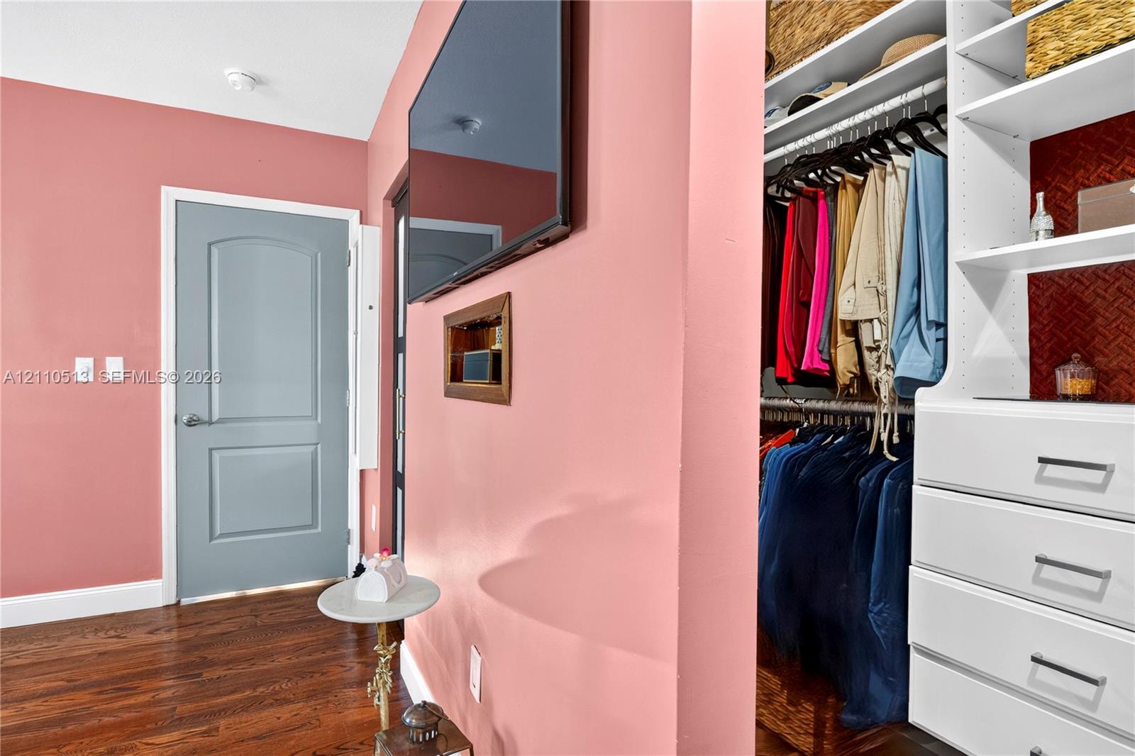 Custom built-in closet featuring white cabinetry, multiple shelving tiers, and integrated drawers with metal pulls, finished with wood-finish flooring and a paneled interior door