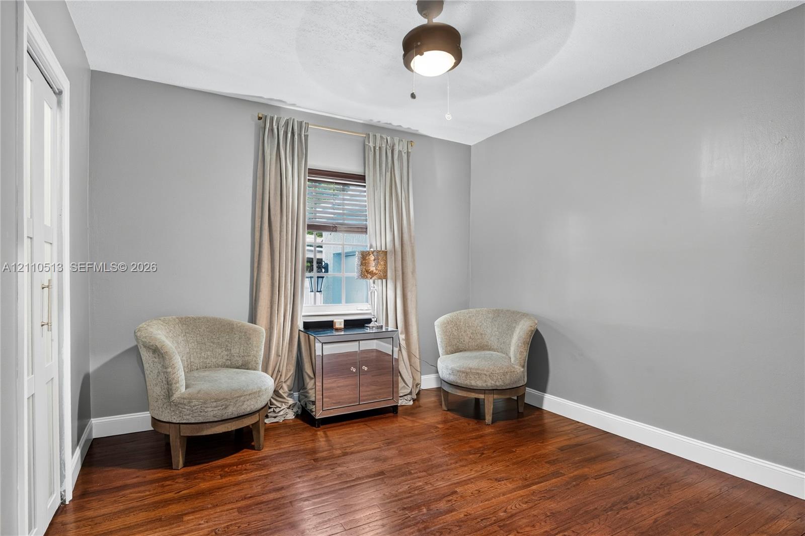 Room featuring wood-finish flooring, a central ceiling fan with an integrated light fixture, and a window with white trim