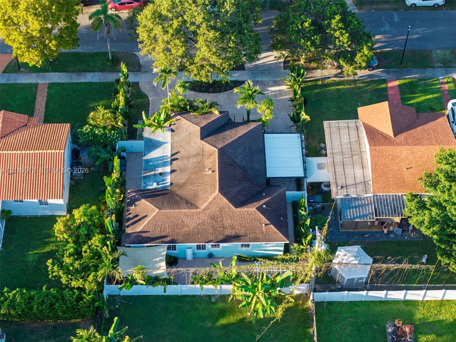 Aerial perspective featuring a multi-hipped roofline, paved driveway, covered patio area, white vinyl perimeter fencing, and mature landscaping Aerial perspective featuring a multi-hipped roofline, paved driveway, covered patio area, white vinyl perimeter fencing, and mature landscaping
