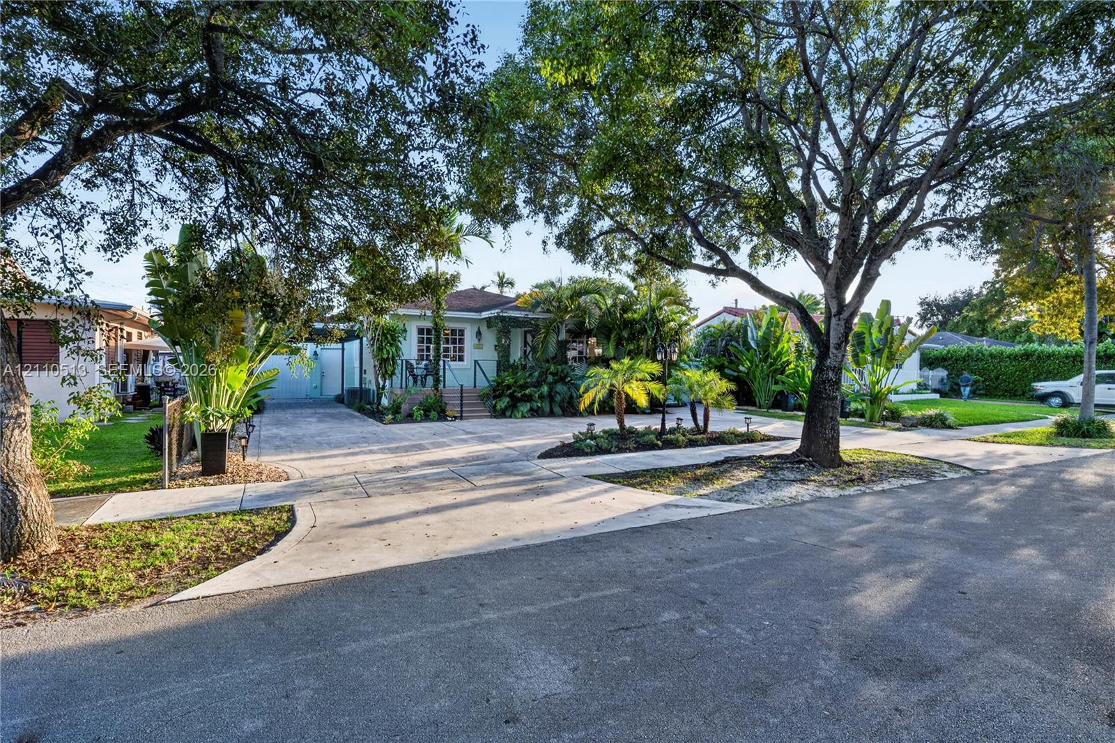 Exterior featuring a concrete driveway, mature canopy trees, lush tropical landscaping, and a raised front entryway Exterior featuring a concrete driveway, mature canopy trees, lush tropical landscaping, and a raised front entryway