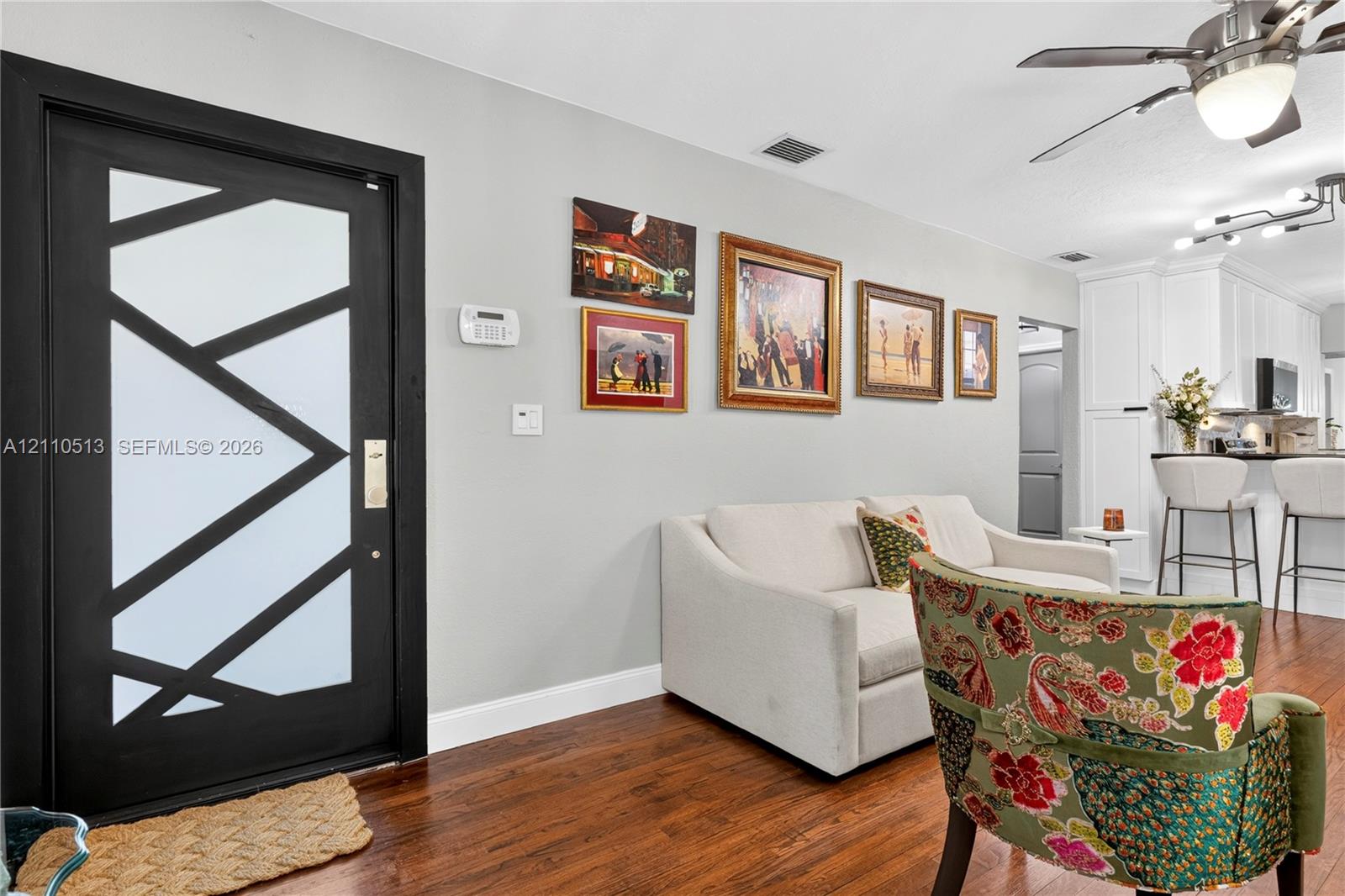 Modern front door with geometric black trim and frosted glass panels, wood-finish flooring, and ceiling fan with integrated lighting