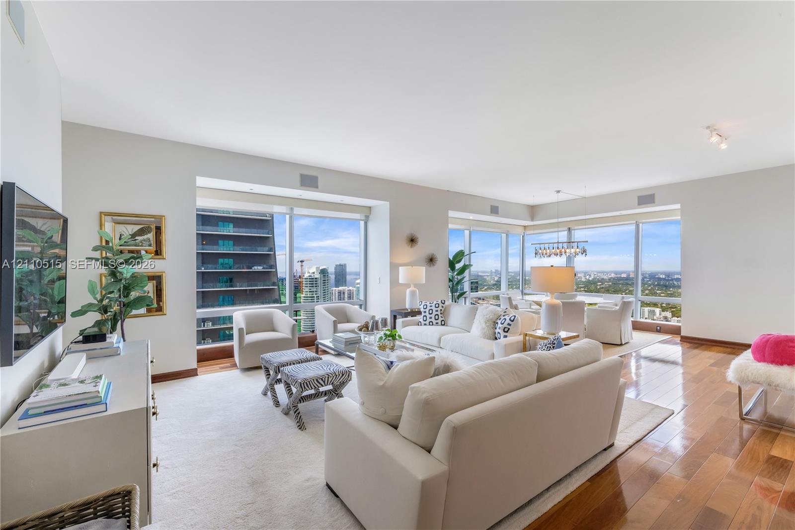 Open-concept living area featuring floor-to-ceiling windows, wood-finish flooring, and high-rise urban scenery