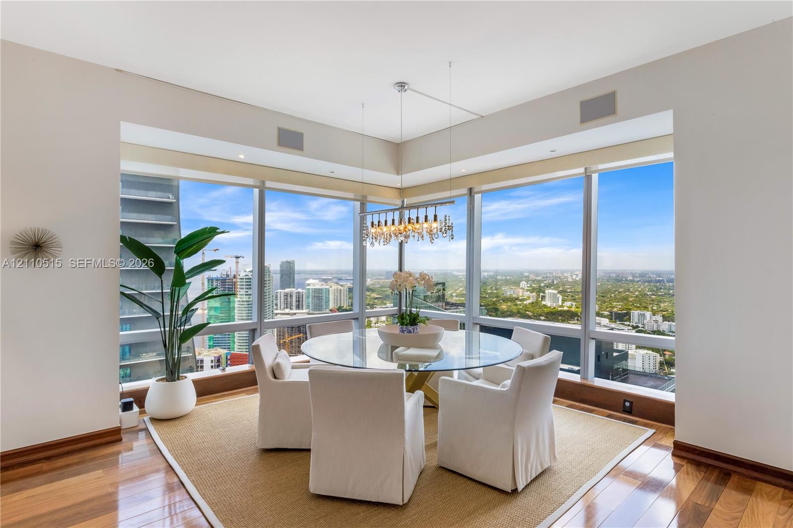 Floor-to-ceiling corner windows with urban and landscape exposure, wood-finish flooring, and a multi-light suspended chandelier fixture