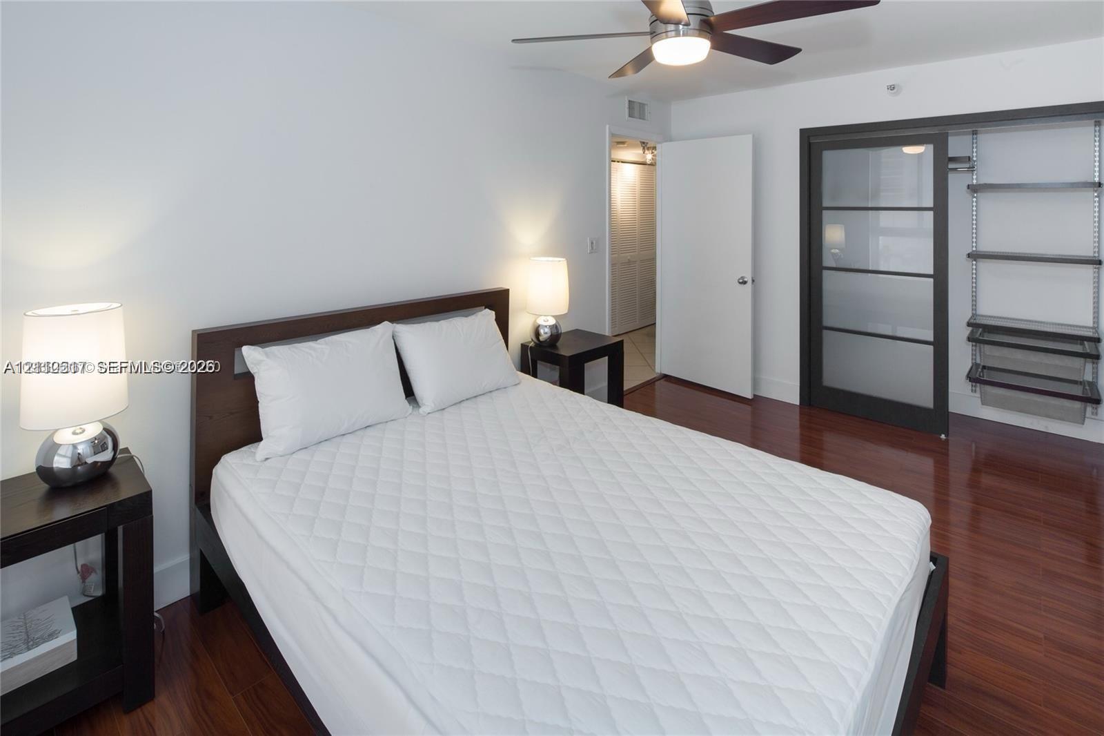 Wood-finish flooring, ceiling fan with integrated lighting, and closet featuring a dark-frame sliding glass door and built-in shelving Wood-finish flooring, ceiling fan with integrated lighting, and closet featuring a dark-frame sliding glass door and built-in shelving