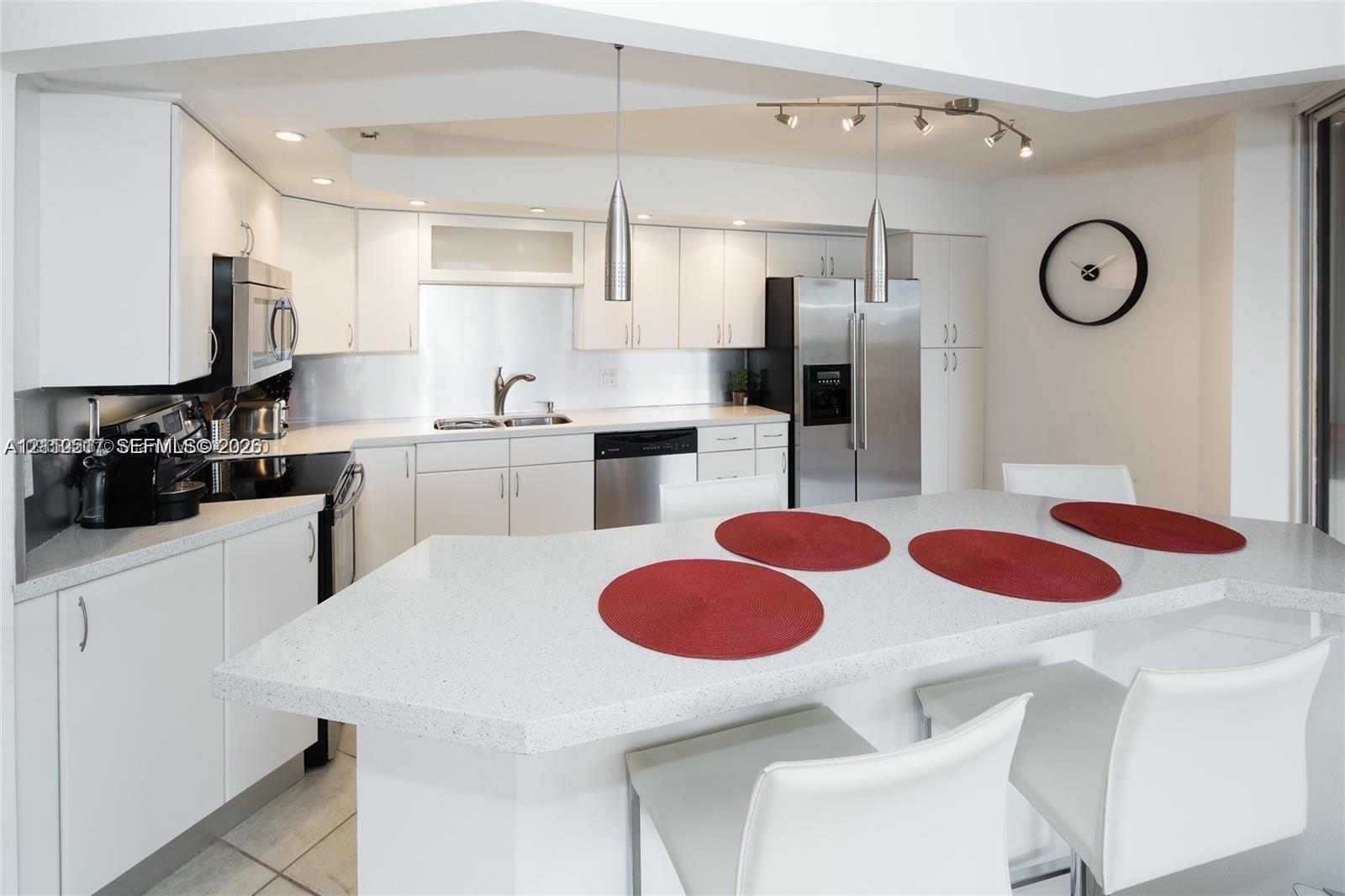 Kitchen featuring flat-panel white cabinetry, solid-surface countertops with an integrated breakfast bar, stainless steel appliances, and dual pendant lighting Kitchen featuring flat-panel white cabinetry, solid-surface countertops with an integrated breakfast bar, stainless steel appliances, and dual pendant lighting